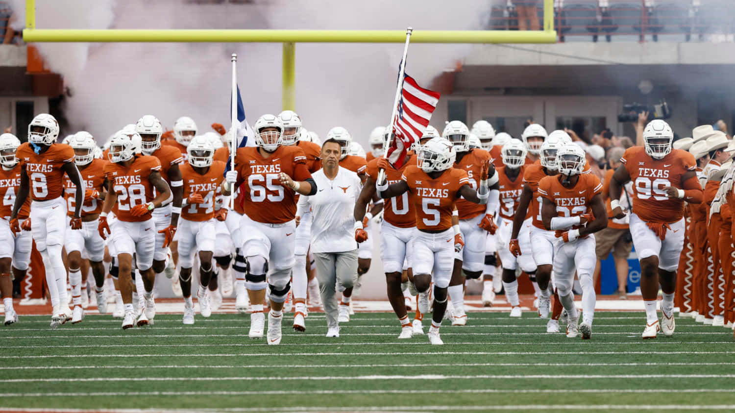 Texas Football 桌布 壁紙 — 德州長角牛美式足球隊身穿橙色和白色球衣，在煙霧繚繞中跑入球場。