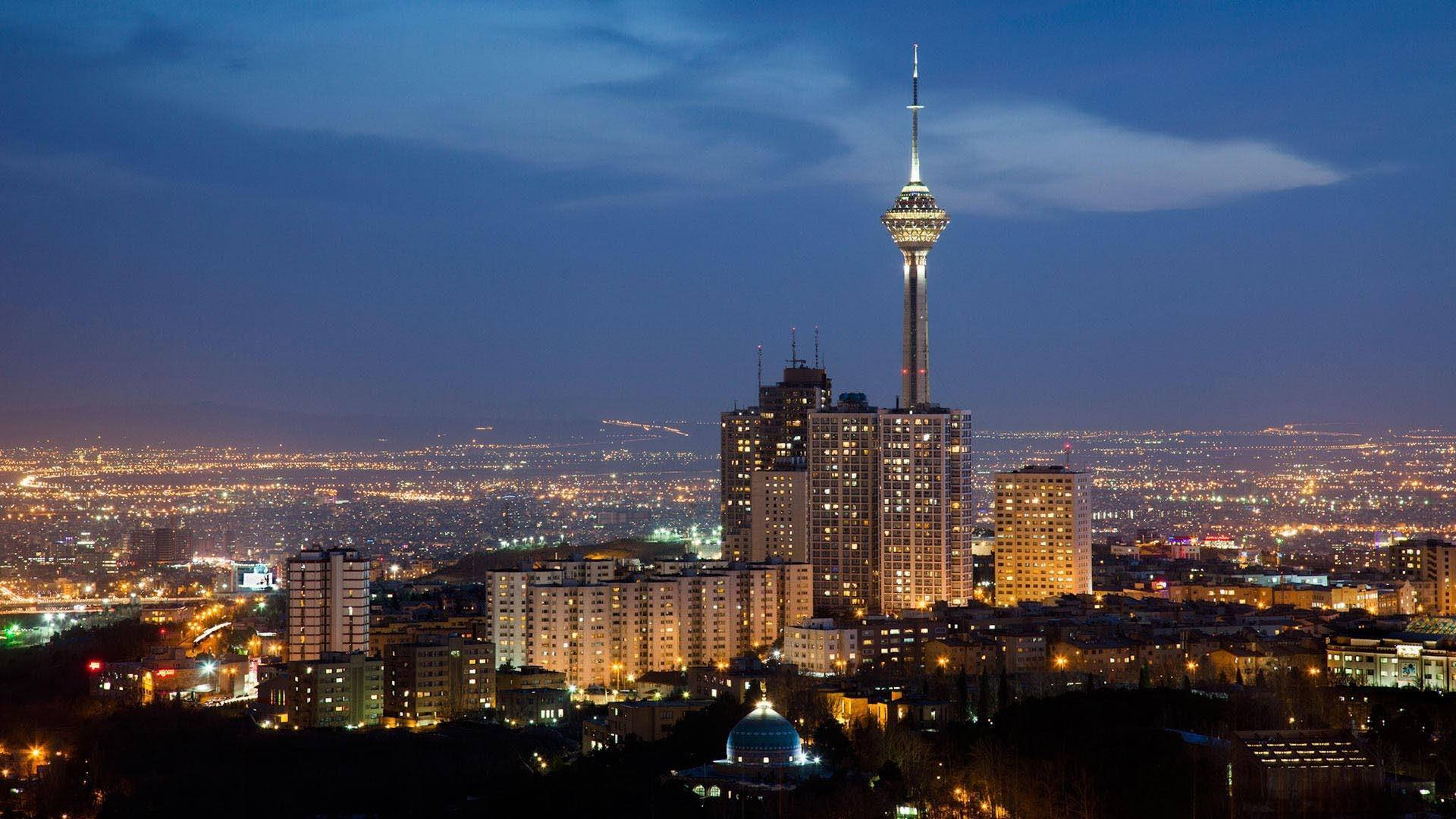 德黑蘭 桌布 壁紙 — 德黑蘭天際線的 panoramic 夜景，以燈火通明的米拉德塔和深藍色天空下蔓延的城市燈光為主導。