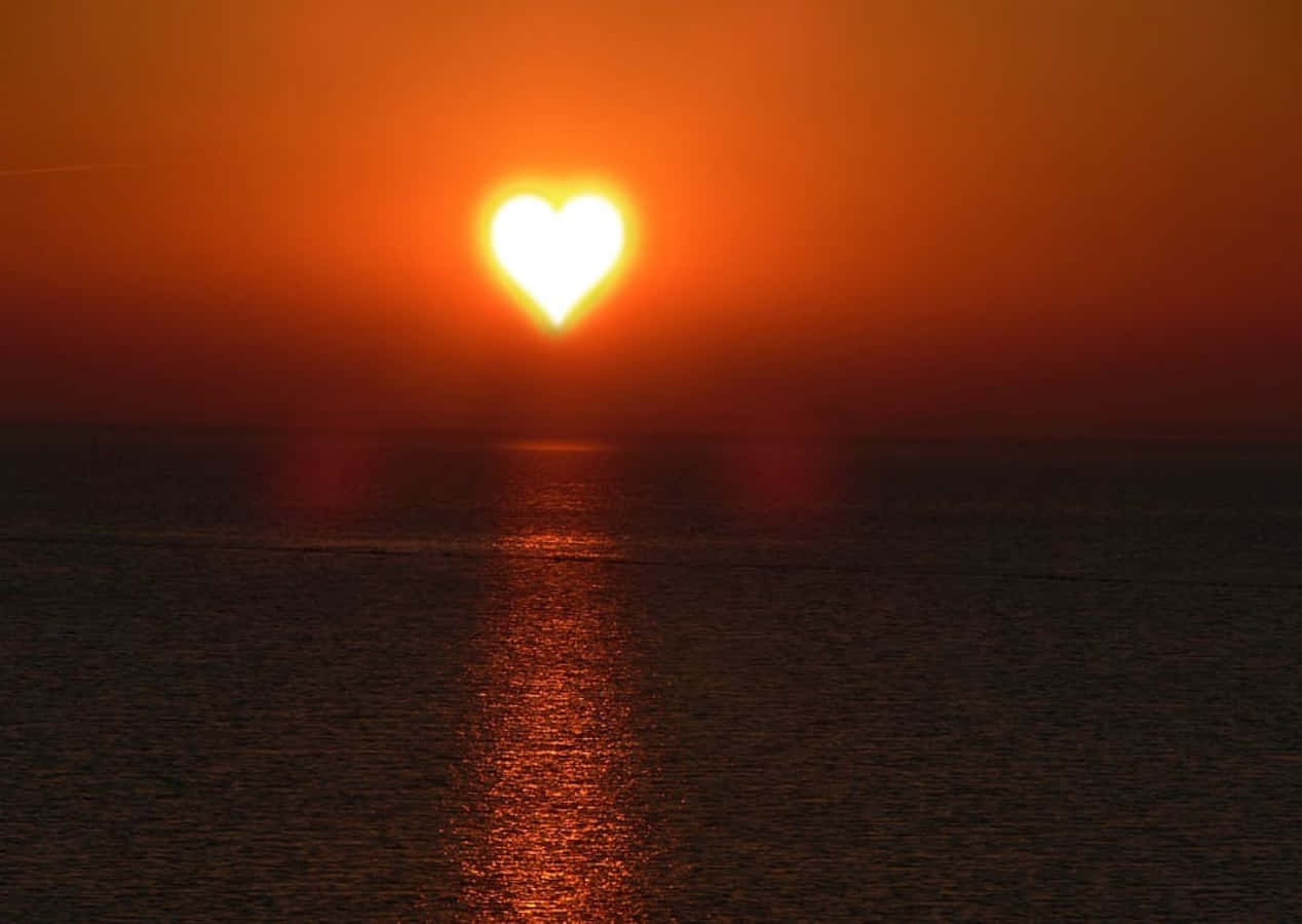 Heart Silhouette 桌布 壁紙 — 心形太陽在日落時溫暖地照耀著平靜的海洋，在水面上投射出火紅色的橙色倒影。