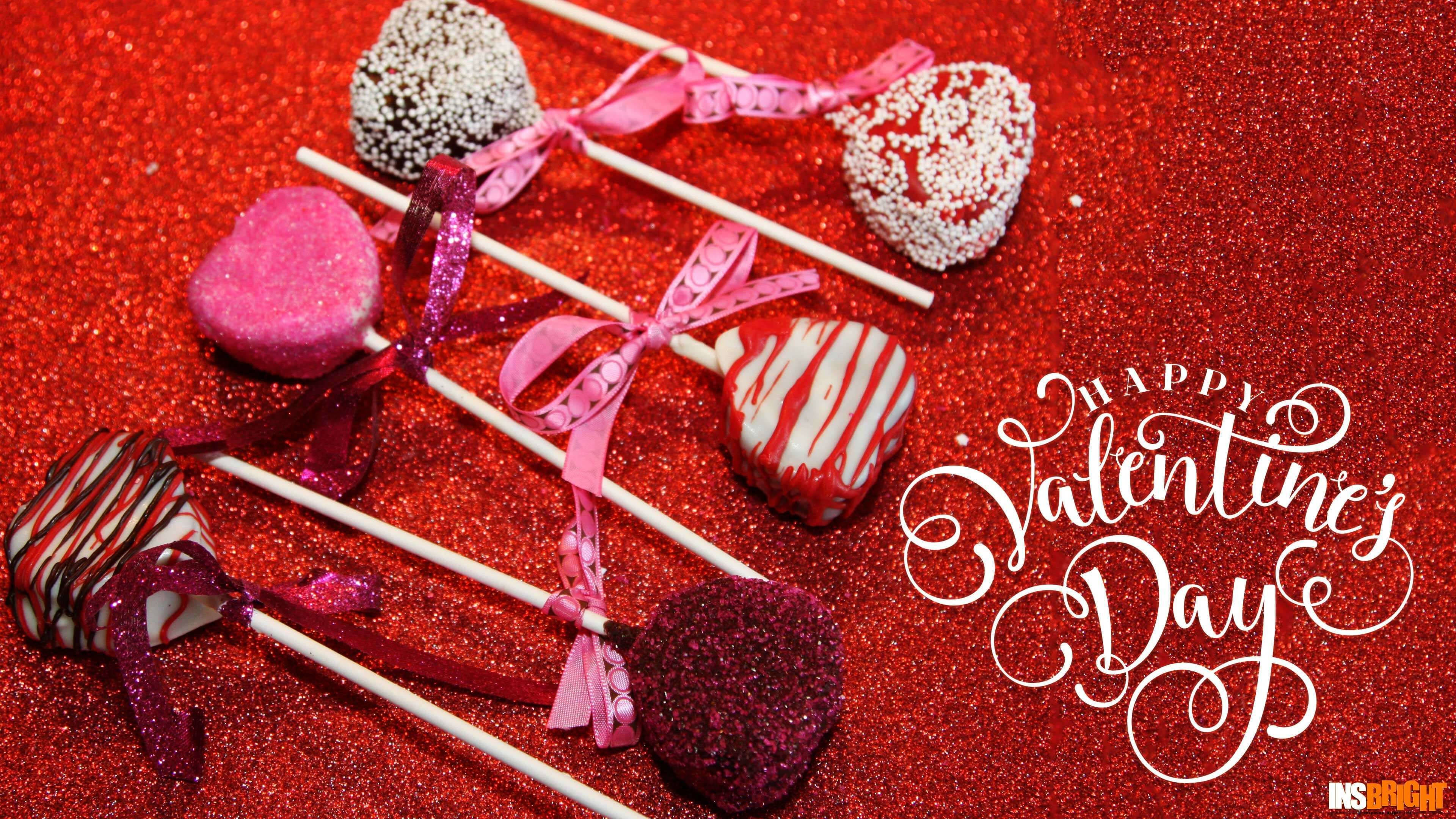 Valentines 桌布 壁紙 — 心形巧克力棒棒糖配上粉紅絲帶，放在閃爍的紅色背景上，旁邊有優雅的情人節字句。
