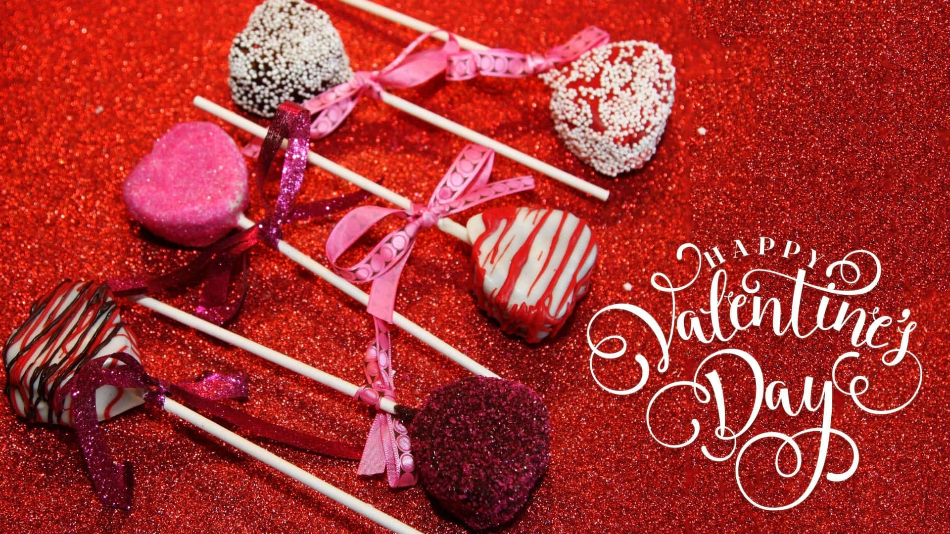 happy valentine's day 桌布 壁紙 — 心形巧克力棒棒糖飾有亮粉和絲帶，放在閃亮的紅色表面上，旁邊是優雅的白色情人節字體。