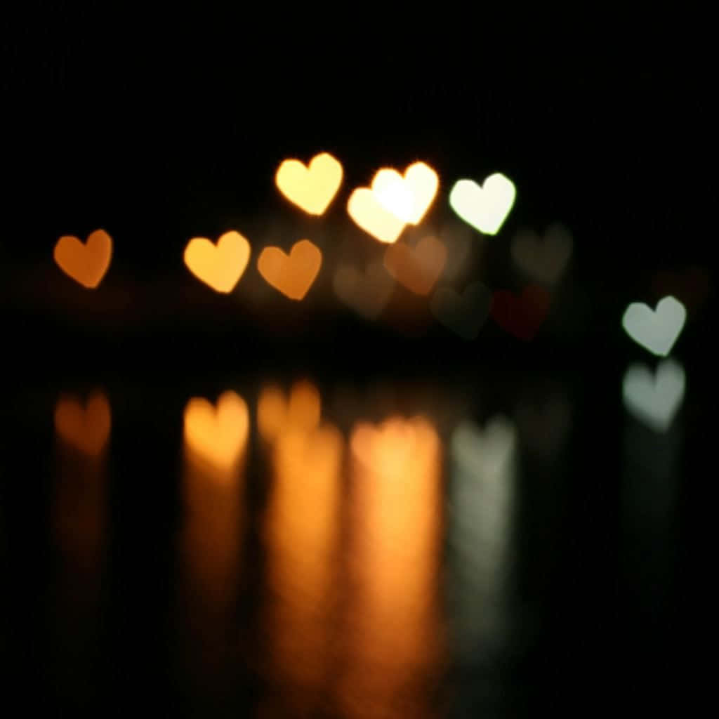 Orange Heart 桌布 壁紙 — 心形散景燈光在黑暗的水面上溫暖地發光，反射出柔和的金色和白色色調。