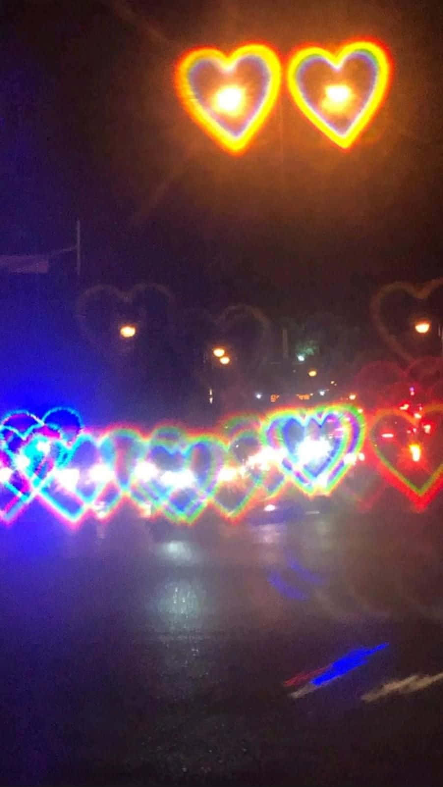 心形美學 桌布 壁紙 — 心形燈光劃過濕漉漉的夜晚街道，反射出過往車輛的鮮豔彩虹色調。