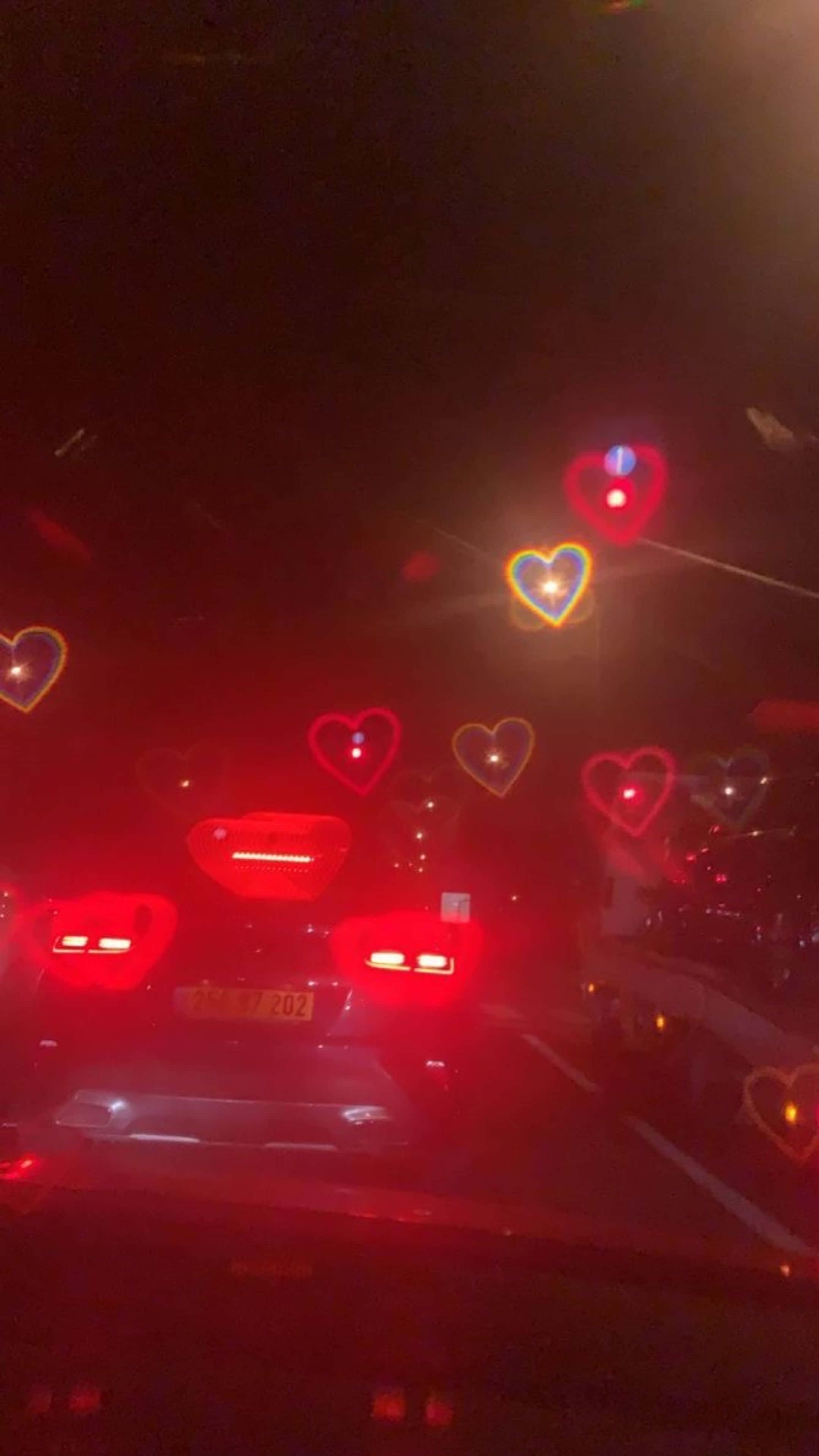 Red Hearts 桌布 壁紙 — 心形燈光在黑暗的夜空中發出紅色和黃色的光芒，映照在道路上汽車的煞車燈上方。