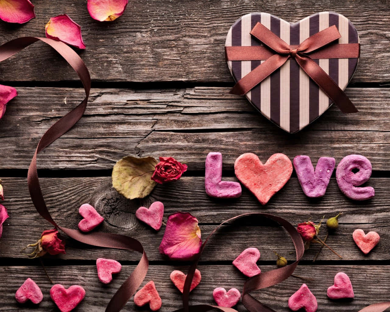 Valentine Day 桌布 壁紙 — 心形禮物盒和粉紅色黏土心形在質樸的木質表面上拼出「love」，並配有玫瑰花瓣和絲帶。