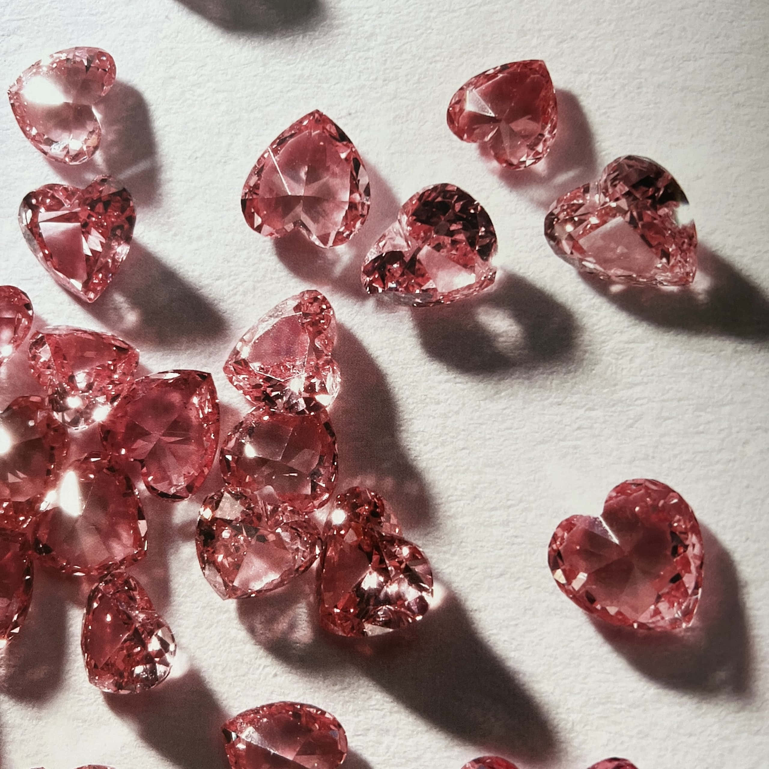 Pink Diamond 桌布 壁紙 — 心形粉紅寶石在柔和白色紋理表面上，於戲劇性燈光下閃爍著銳利切面。
