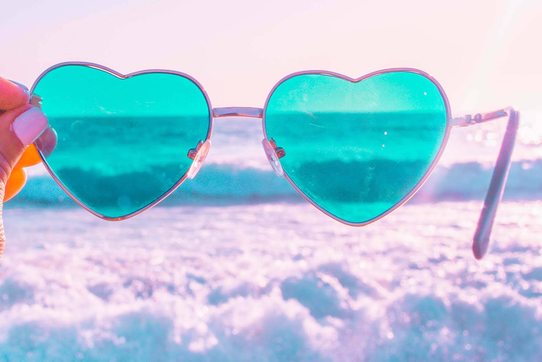 手裡拿著心形太陽眼鏡，在粉彩海灘上反射著海浪。