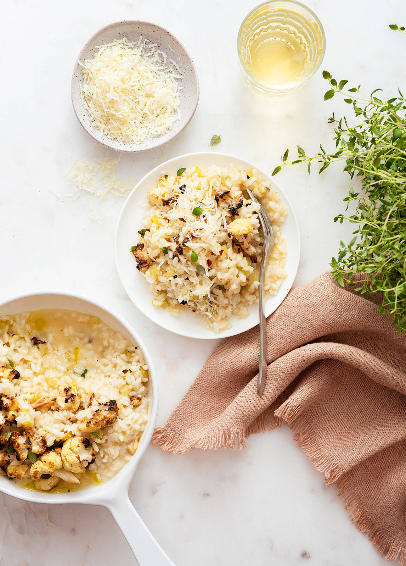 Healthy Food 桌布 壁紙 — 忌廉狀的義大利燴飯配烤白花椰菜和新鮮百里香，盛載於白色煎鍋和碗中，置於大理石表面，附有粉紅色餐巾和一杯葡萄酒。