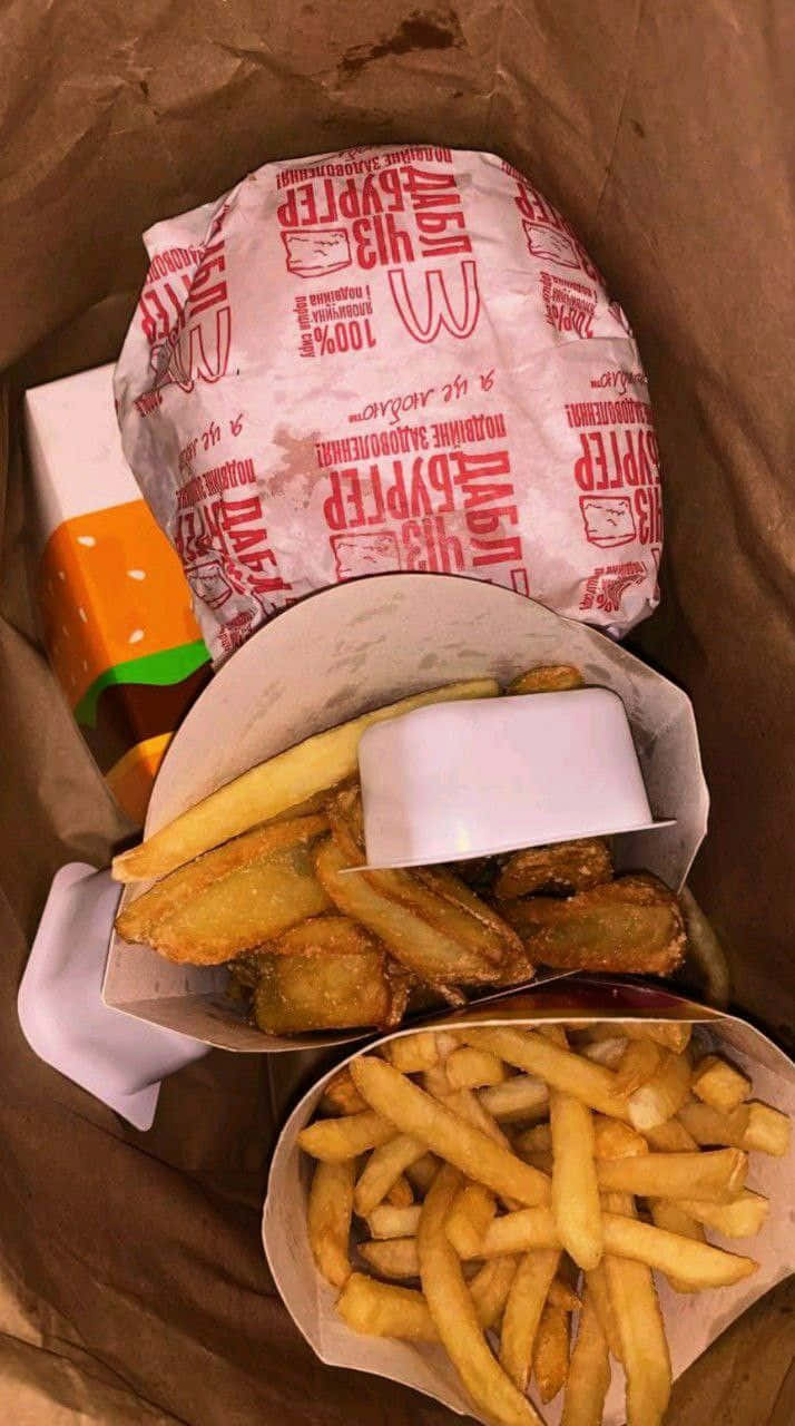 Fries 桌布 壁紙 — 快餐餐點的近距離特寫，包括一個用品牌紙包裹的漢堡和兩份放在紙籃裡的金黃色薯條。