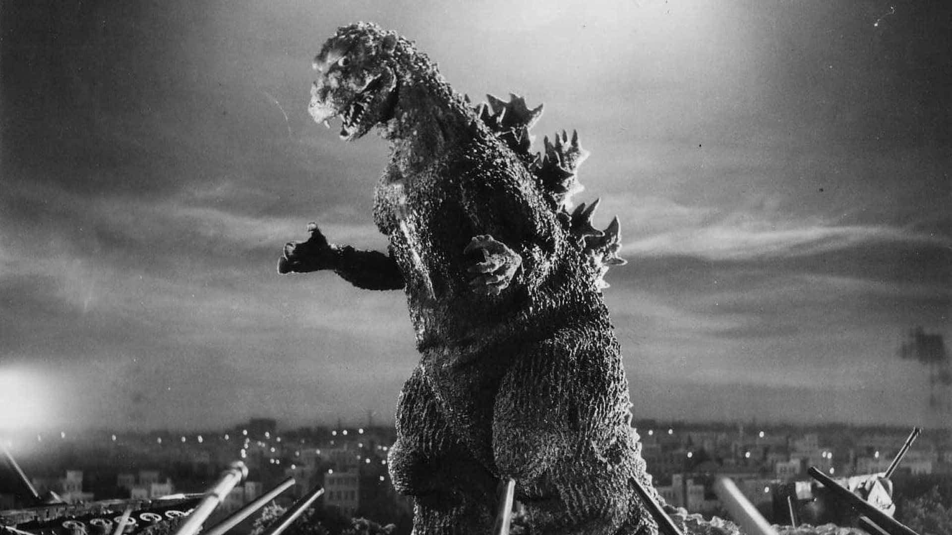 Classic Godzilla 桌布 壁紙 — 怪獸哥吉拉在夜晚站在廢墟城市景觀之上，發光的眼睛和尖刺背部映襯著多雲的天空。