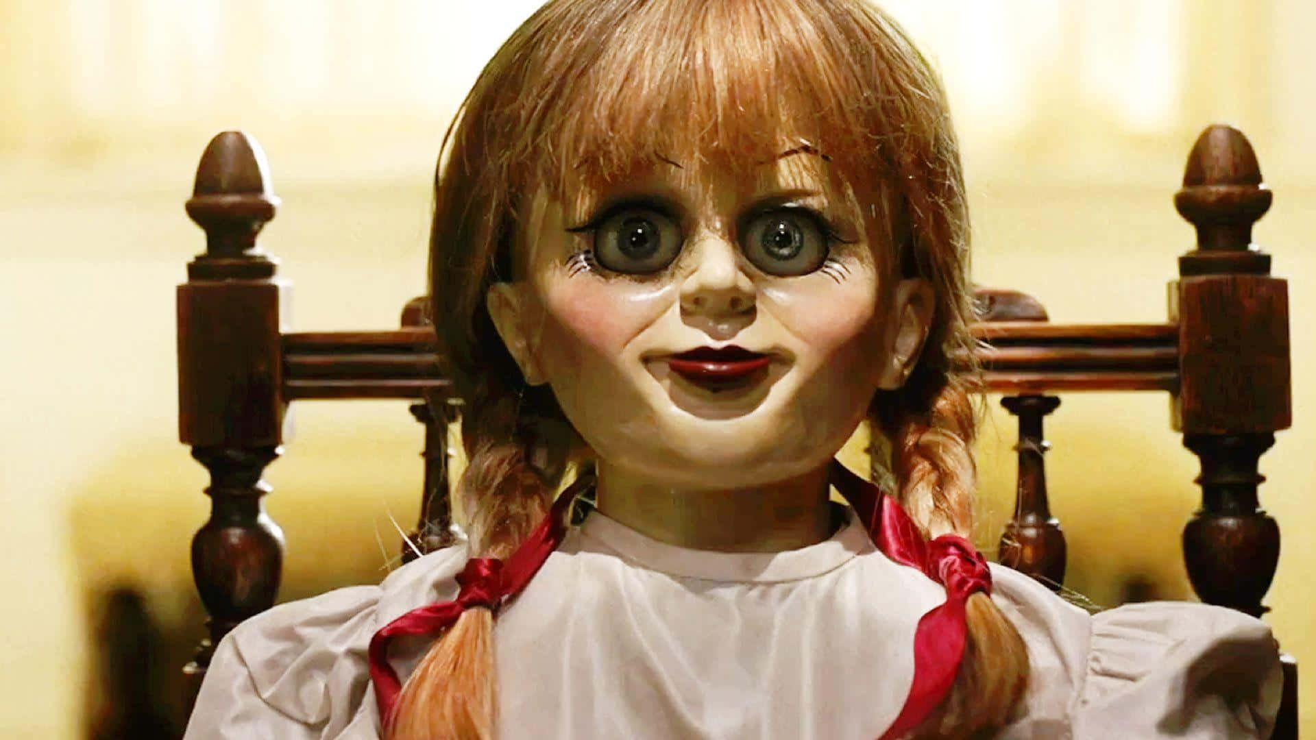 Annabelle 桌布 壁紙 — 恐怖娃娃安娜貝爾的特寫，有著寬大的玻璃眼睛和紅色絲帶，坐在木椅上。