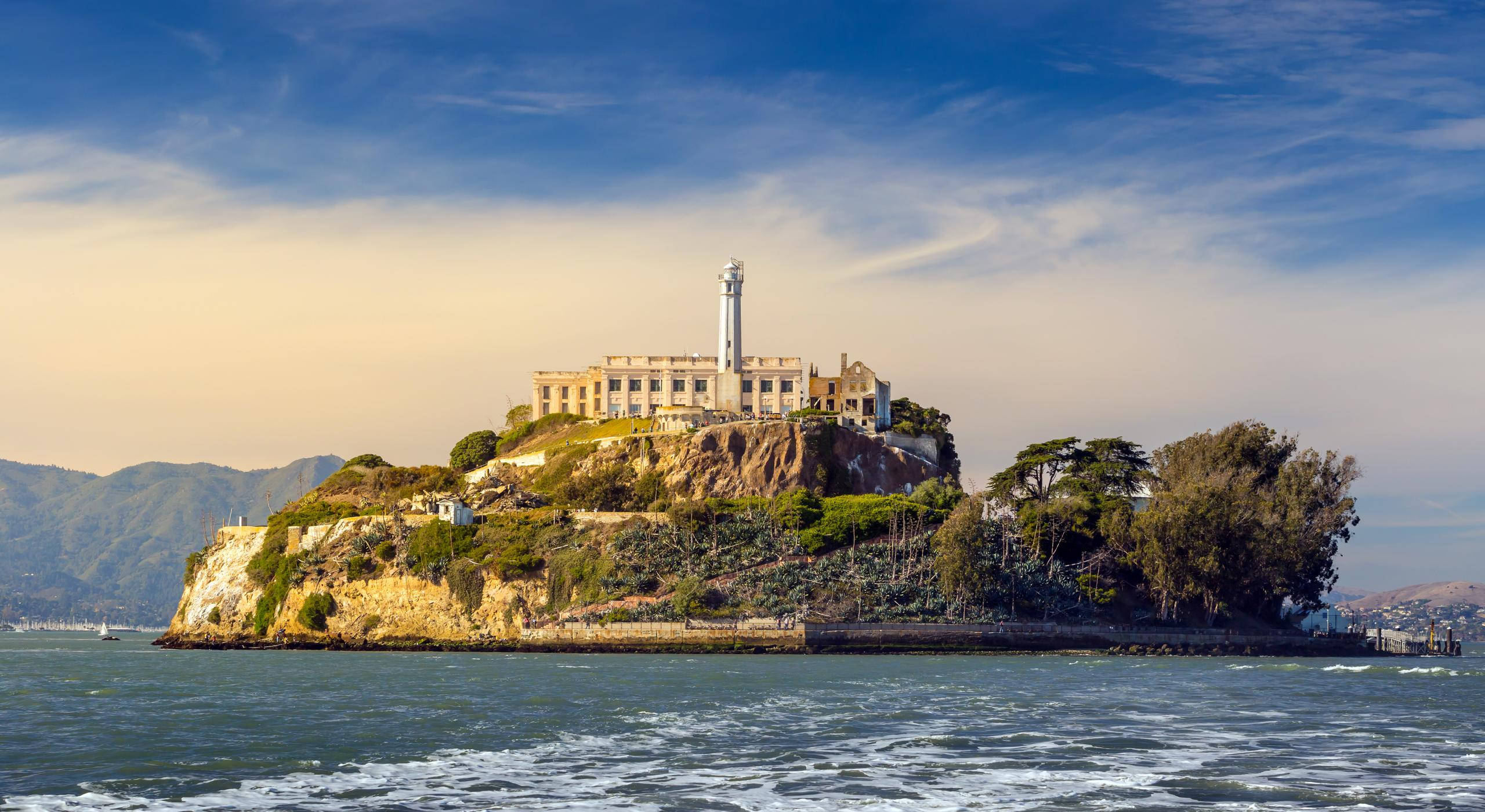San Francisco 桌布 壁紙 — 惡魔島及其歷史悠久的監獄和燈塔，在蔚藍的天空和縷縷白雲下，孤立於海灣中。