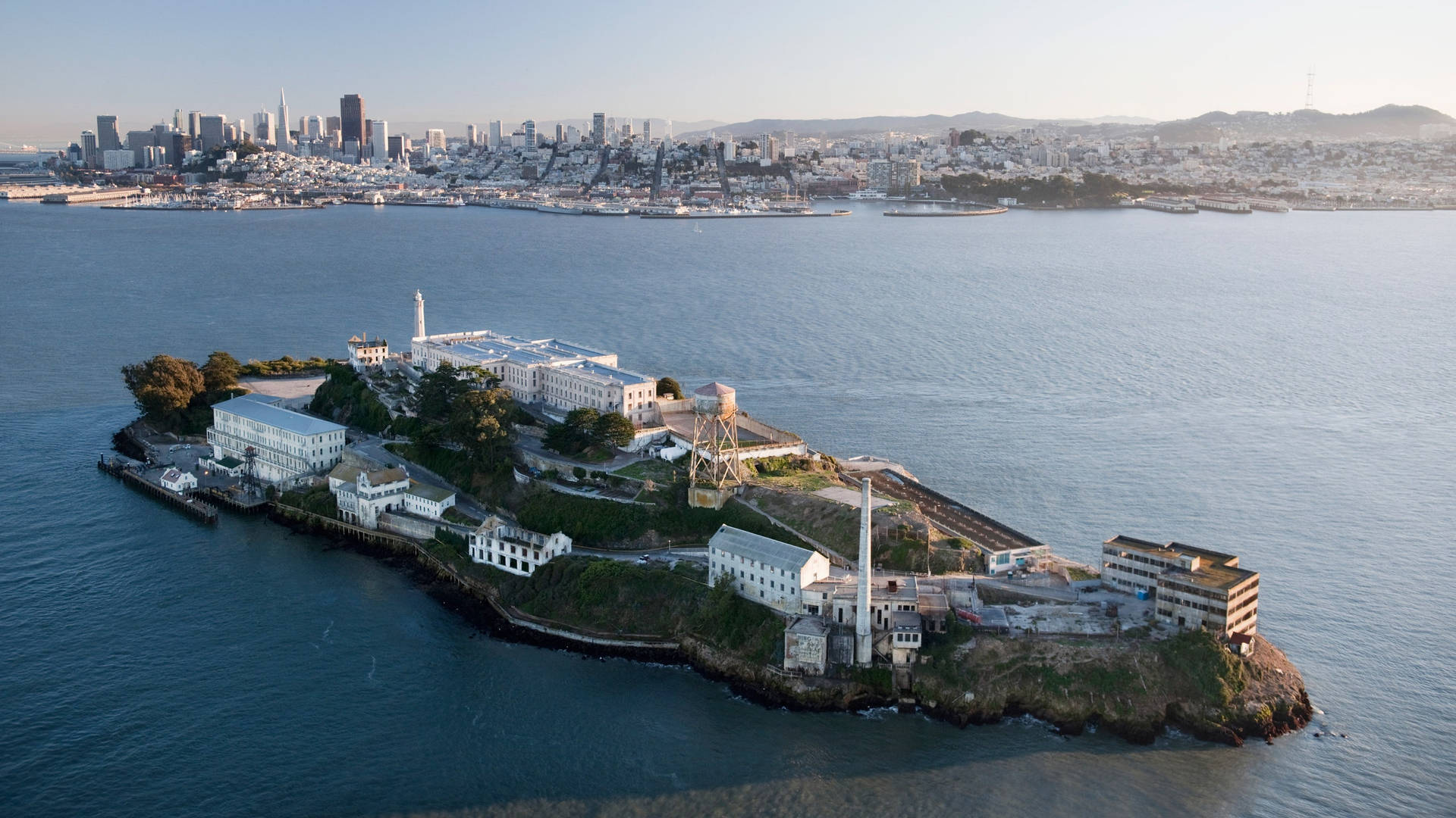 USA 桌布 壁紙 — 惡魔島的鳥瞰圖，歷史監獄建築被深藍色海水包圍，背景是舊金山的天際線。