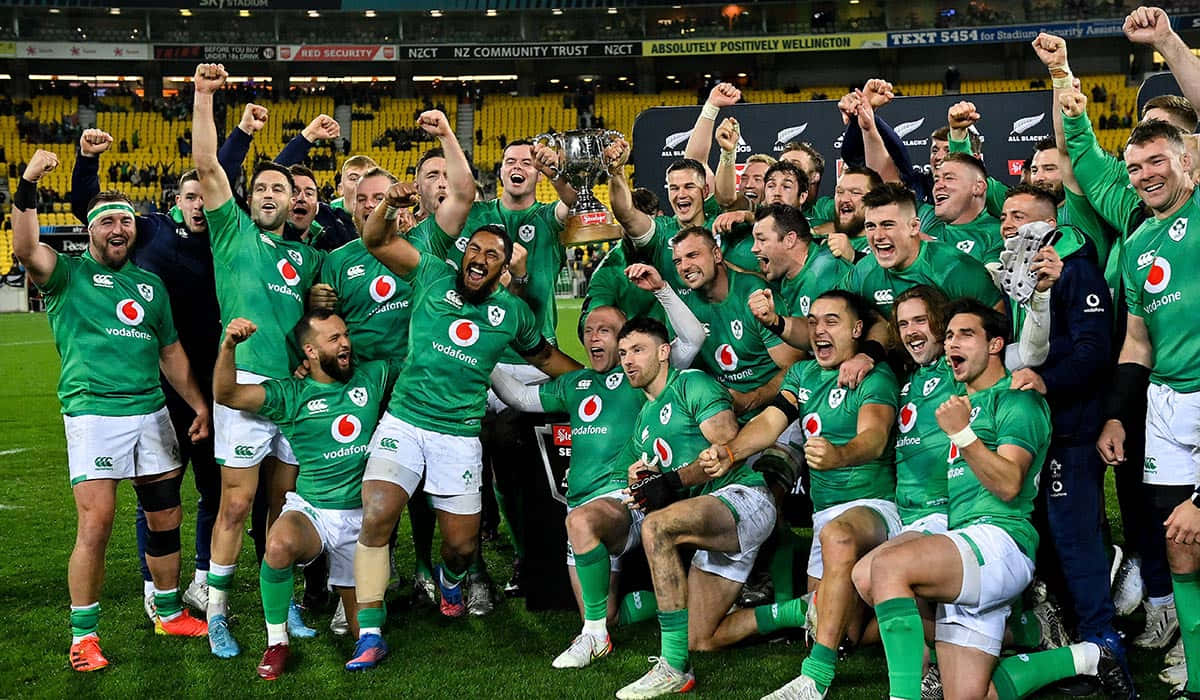 Ireland Rugby 桌布 壁紙 — 愛爾蘭橄欖球隊身穿綠色球衣在球場燈光下的草地上高舉獎盃慶祝勝利。