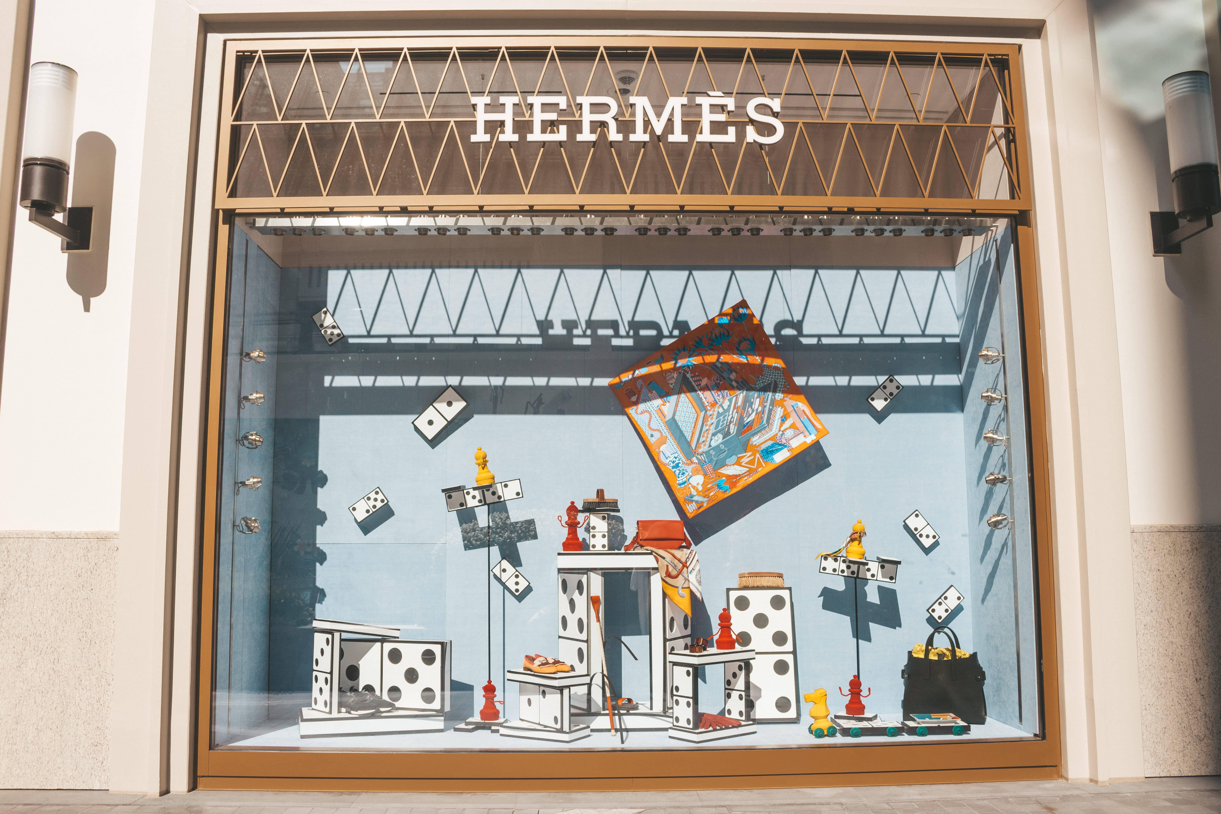 Hermes 桌布 壁紙 — 愛馬仕櫥窗展示以藍色背景襯托玩味十足的多米諾骨牌主題雕塑和彩色絲巾。