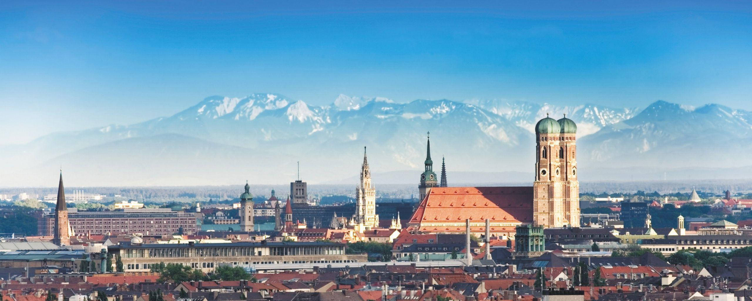 Munich 桌布 壁紙 — 慕尼黑天際線的全景，歷史悠久的教堂和紅色屋頂，背景是白雪覆蓋的阿爾卑斯山，天空清澈湛藍。
