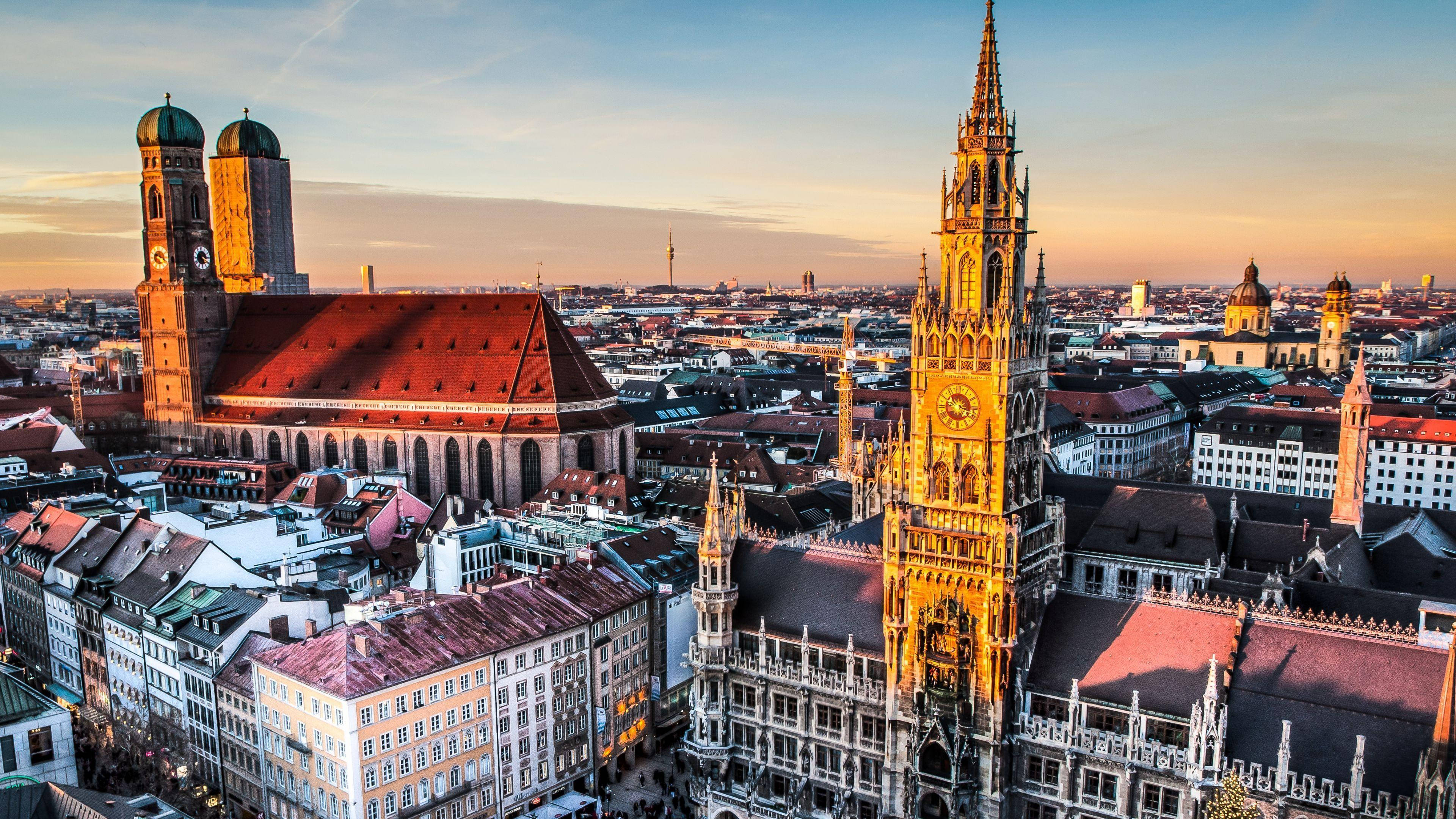 Munich 桌布 壁紙 — 慕尼黑歷史天際線的鳥瞰圖，金色日落突顯聖母教堂和新市政廳，屋頂溫暖發光。