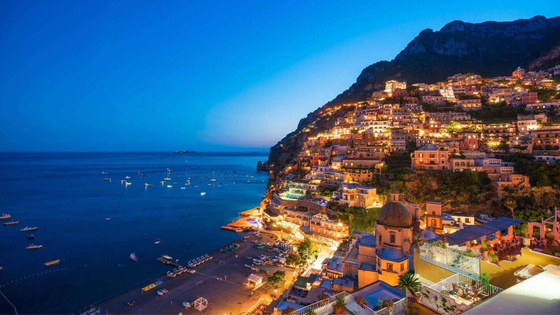 Amalfi Coast 桌布 壁紙 — 懸崖上的沿海小鎮在深藍色的暮色天空和寧靜的海面上閃爍著溫暖的燈光。
