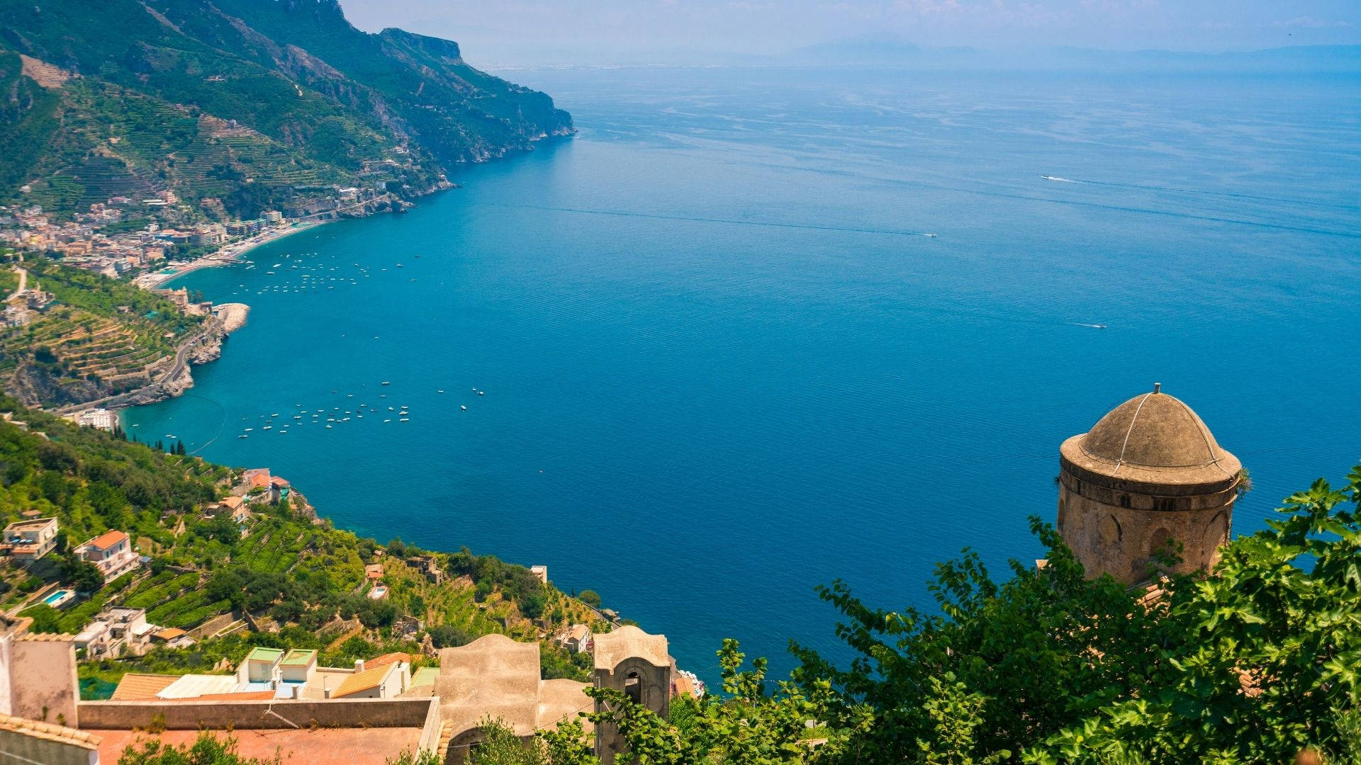 Amalfi Coast 桌布 壁紙 — 懸崖小鎮的壯麗海岸景觀，赤陶屋頂坐落在綠色山丘中，俯瞰廣闊的碧綠海洋。