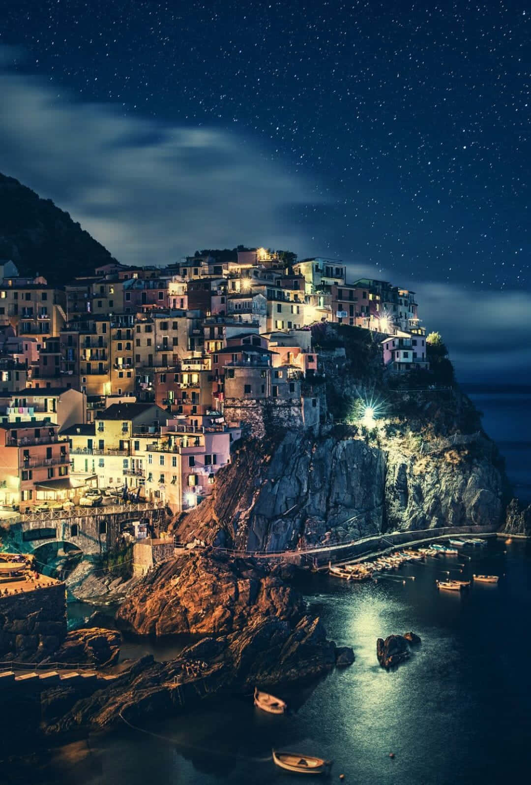 Italy Aesthetic 桌布 壁紙 — 懸崖村莊在深藍色天空和寧靜海面上閃爍著溫暖燈光的星空夜景。