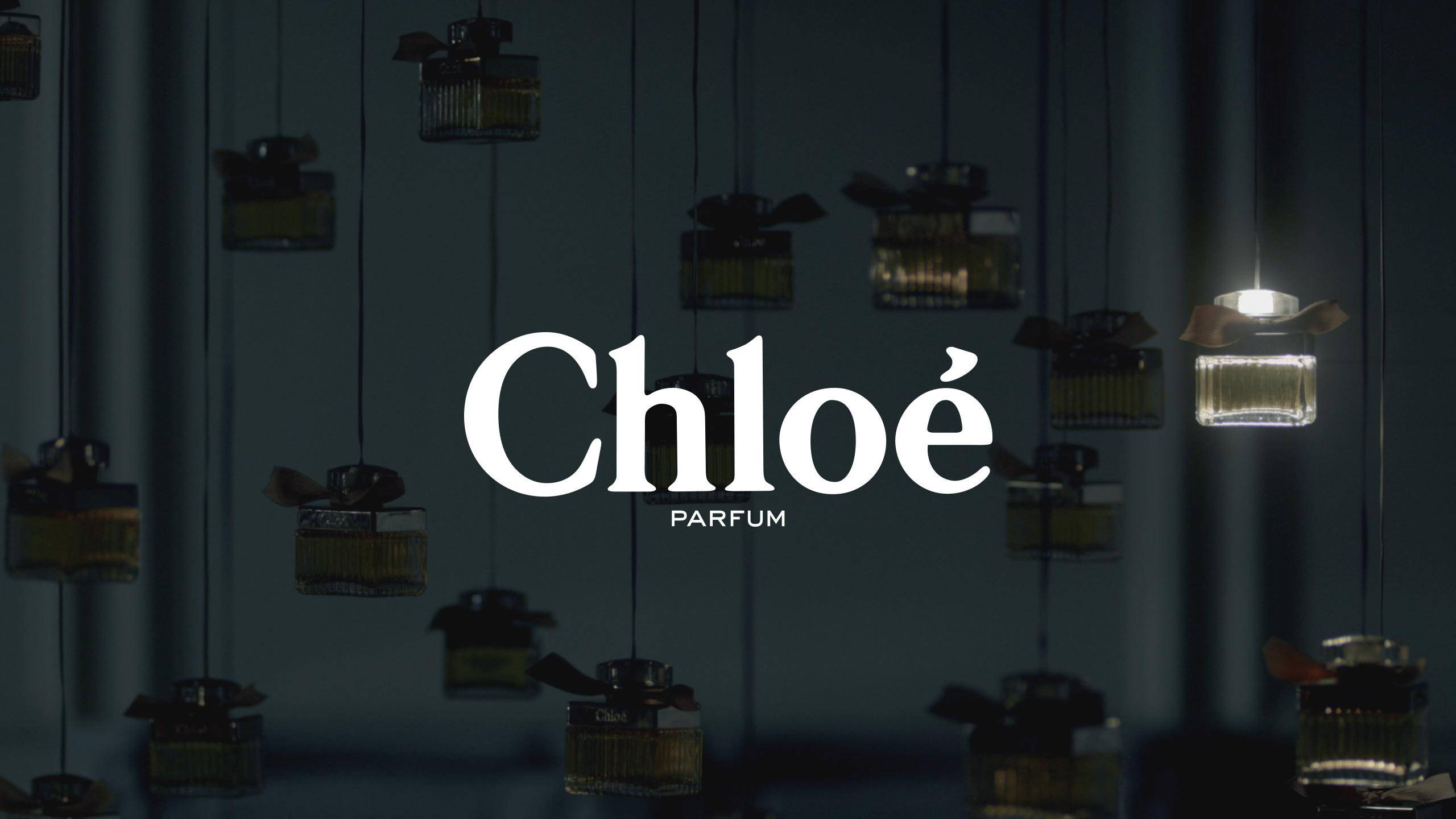品牌 桌布 壁紙 — 懸掛的香水瓶在黑暗背景下柔和發光，品牌名稱 Chloé PARFUM 顯眼展示。