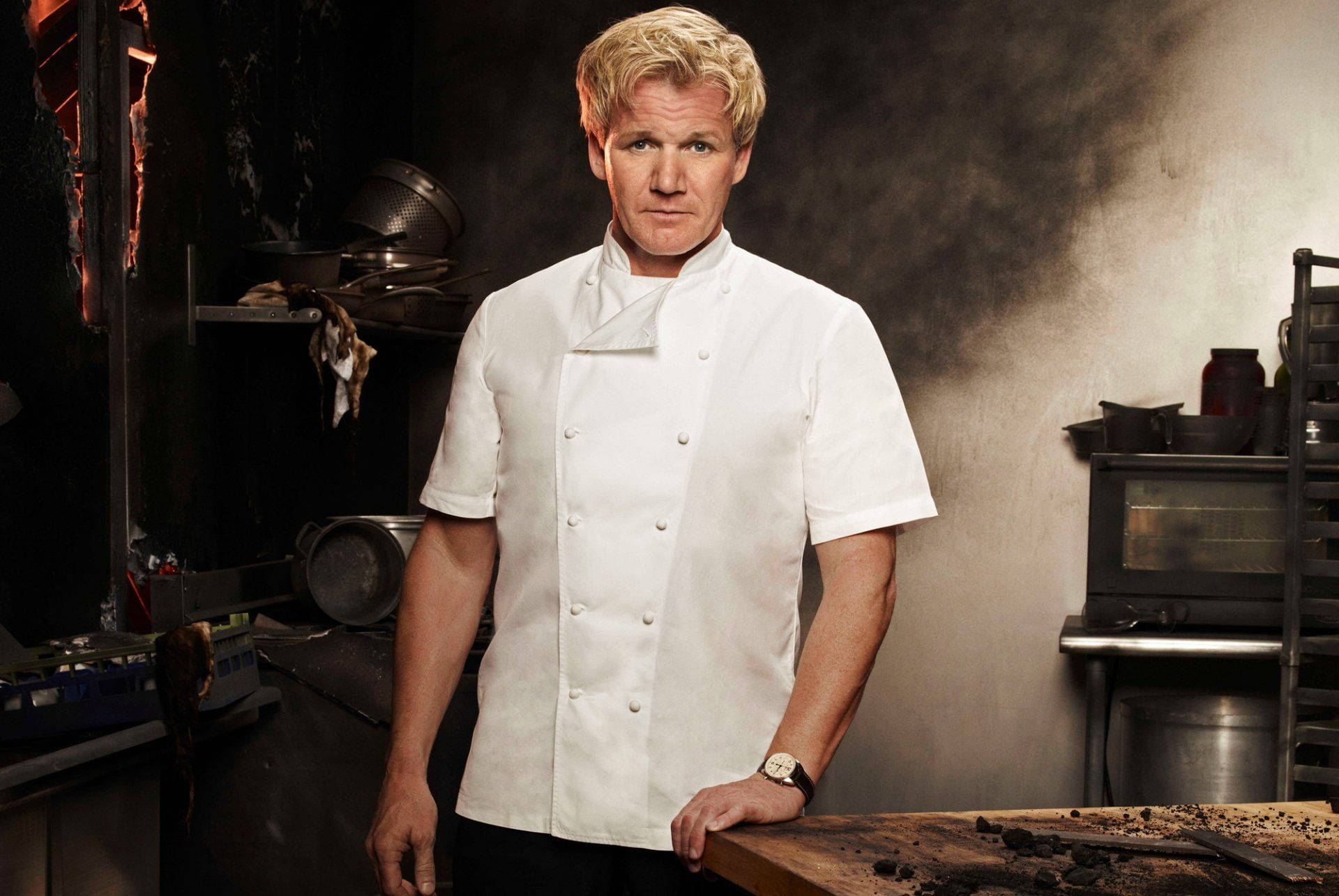 Gordon Ramsay 桌布 壁紙 — 戈登·拉姆齊站在煙霧瀰漫的專業廚房裡，穿著潔白的廚師外套，表情嚴厲。