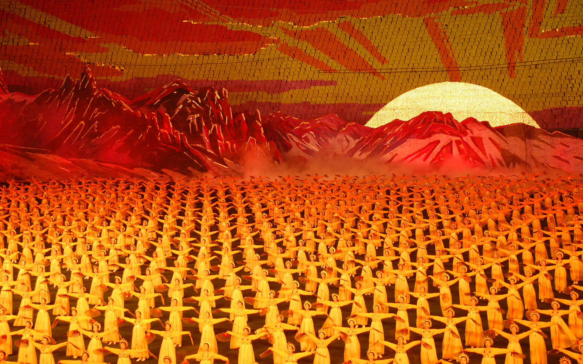 artwork 桌布 壁紙 — 成千上萬身穿金色長袍的表演者，在火紅的山脈背景和閃耀的太陽下，形成同步揮舞手臂的海洋。