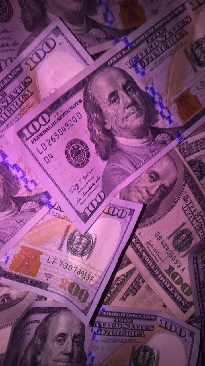 Girly Money 桌布 壁紙 — 成堆的百元美鈔在紫色燈光下發光，營造出奢華而強烈的金融氛圍。