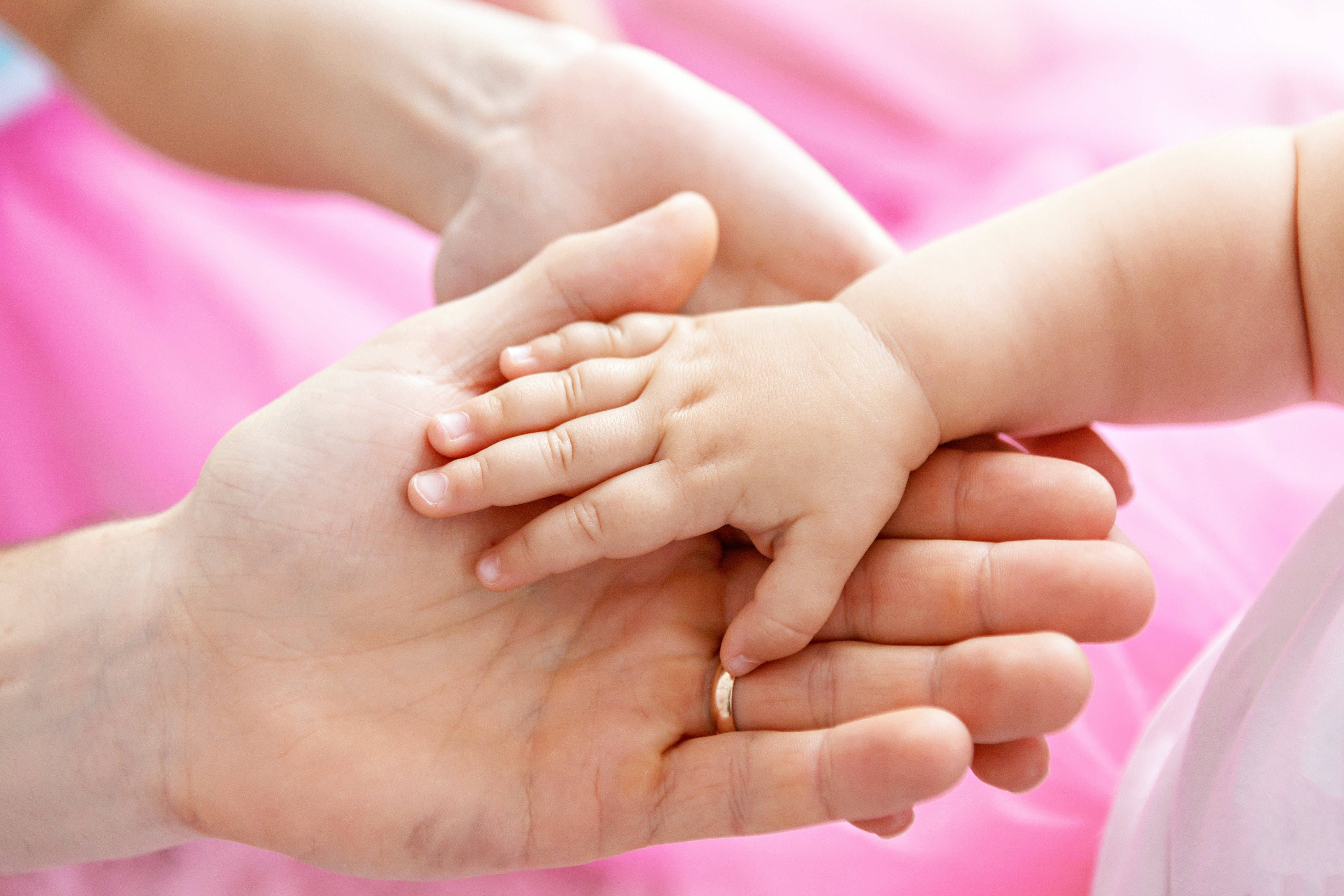 Newborn 桌布 壁紙 — 成年人的手輕輕托住嬰兒的小手，背景是柔和的粉紅色。