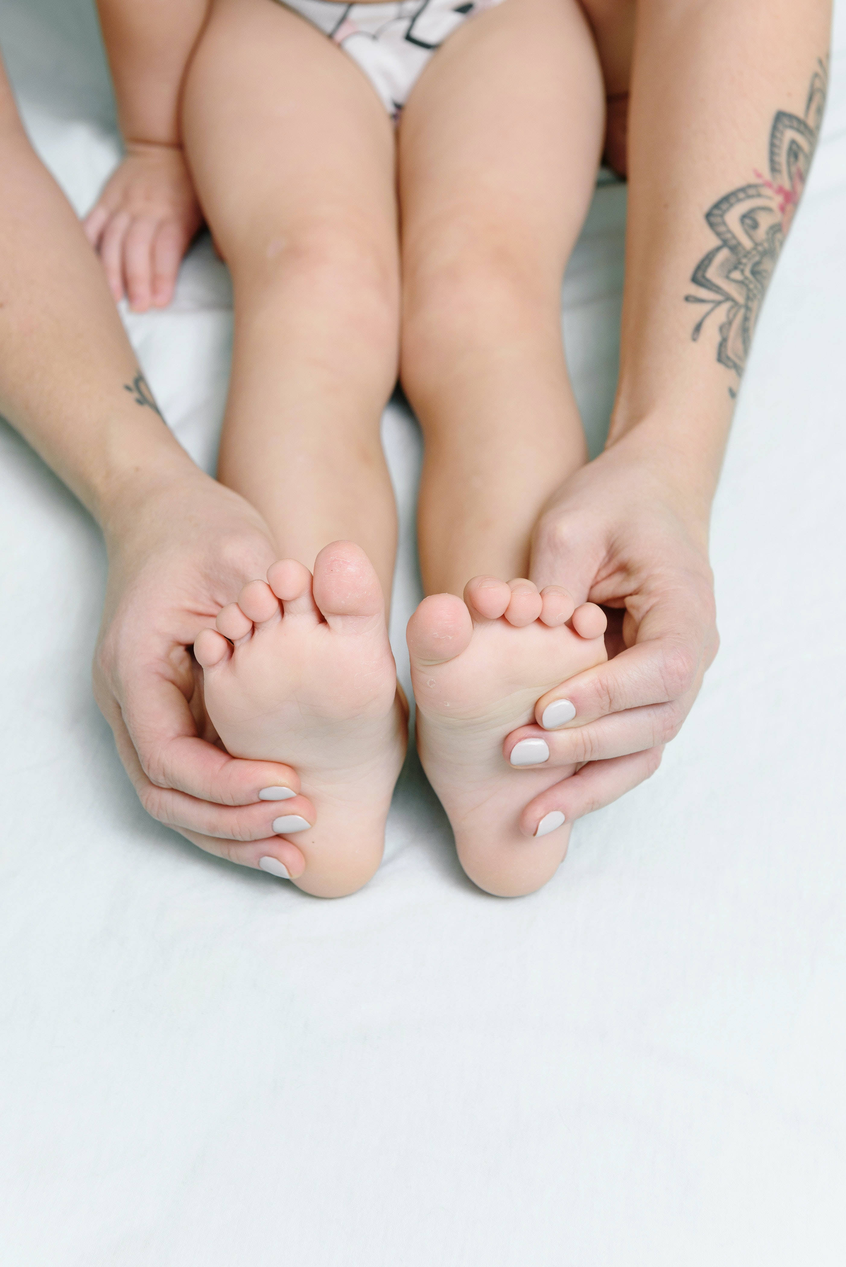 foot massage 桌布 壁紙 — 成年人的手輕輕托著嬰兒的小腳，背景是柔軟的白色。