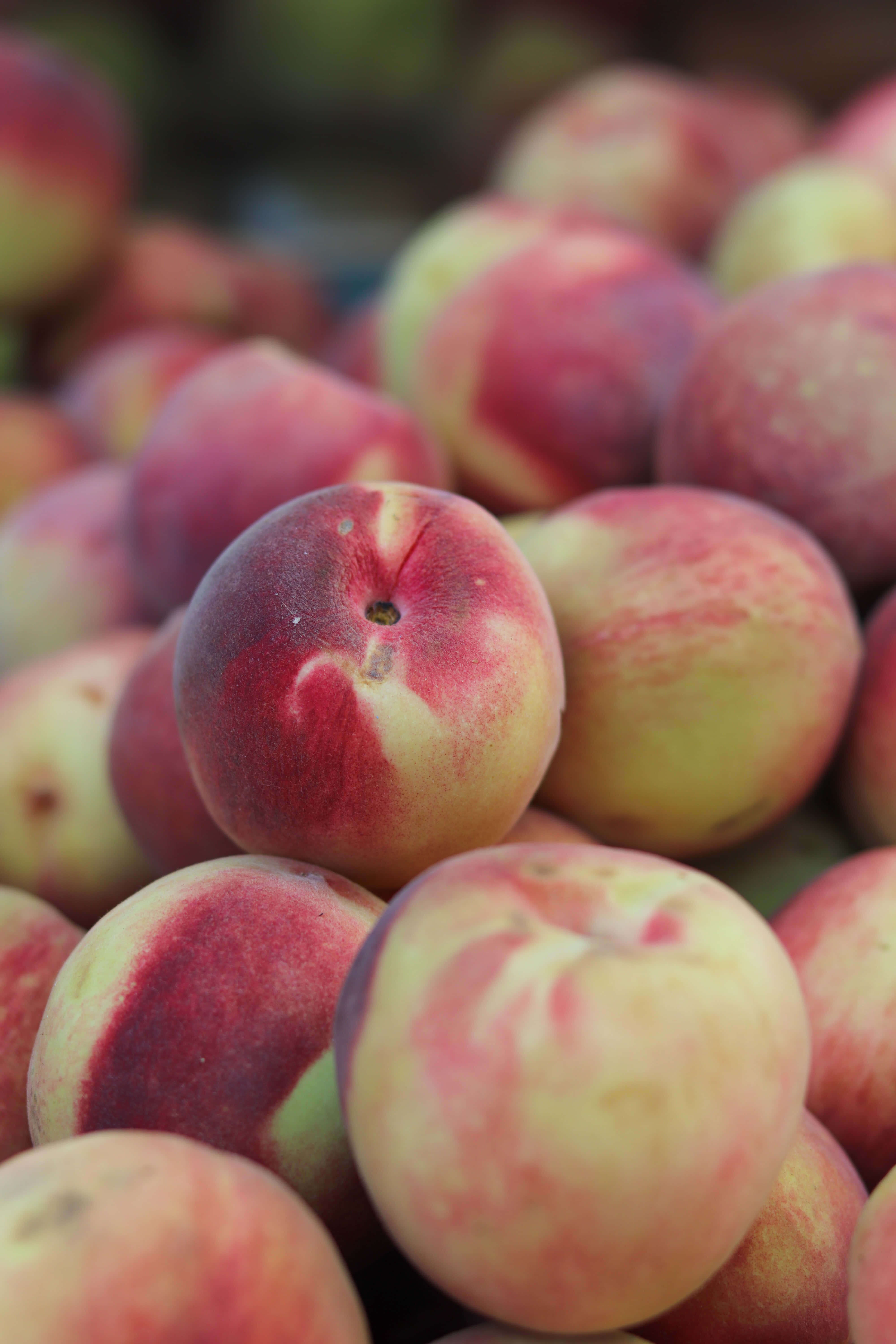 Peaches 桌布 壁紙 — 成熟桃子的特寫，帶有柔和的紅色和黃色色調，堆疊在市場環境中。