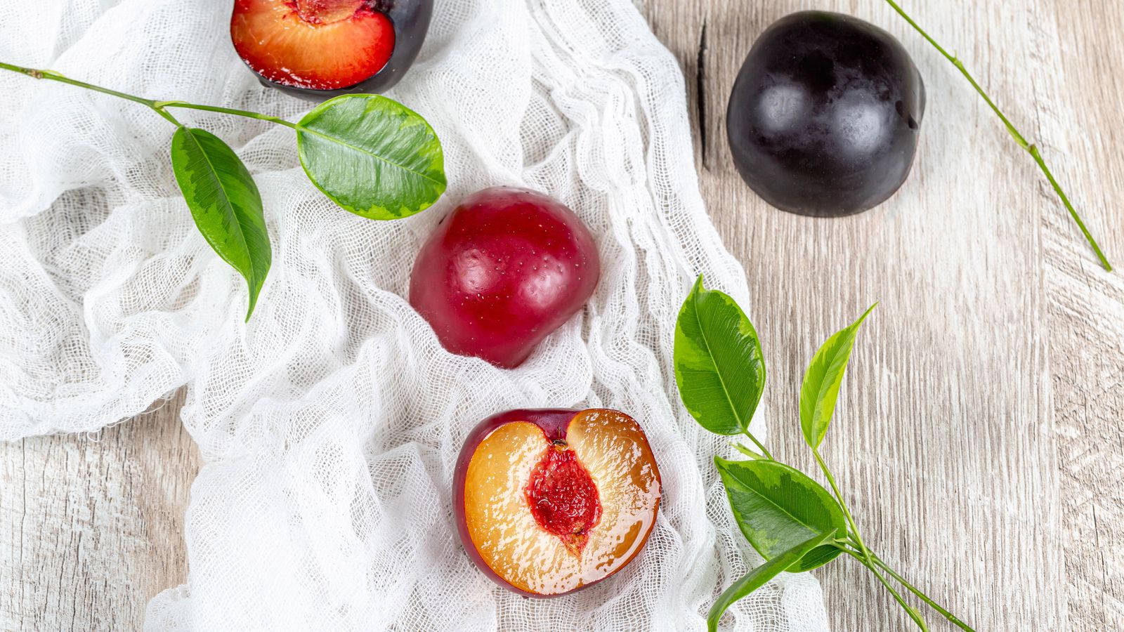 Fruits 桌布 壁紙 — 成熟的李子帶有鮮紅色的果肉和光澤的果皮，放在一塊白布上，置於風化的木質表面。