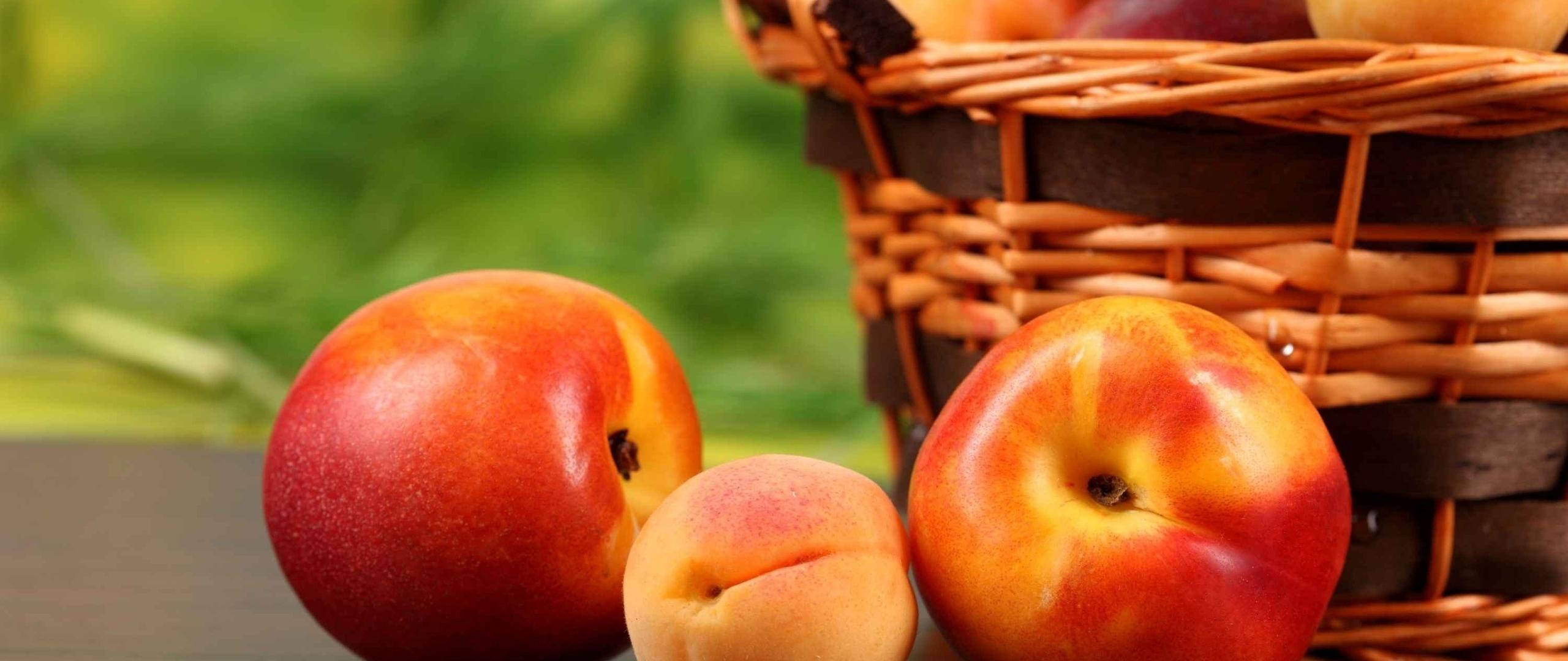 Fruits 桌布 壁紙 — 成熟的桃子帶有絨毛表皮，放在編織籃旁邊，背景是柔和的綠色模糊效果。