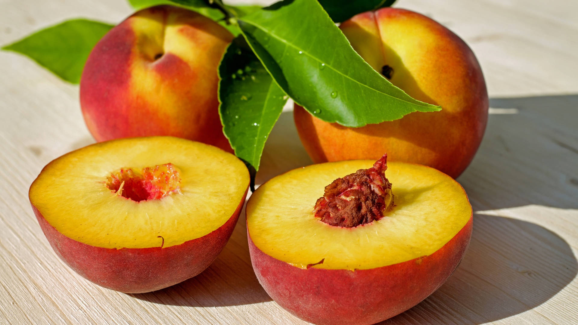 Fruits 桌布 壁紙 — 成熟的水蜜桃帶有鮮豔的紅色和黃色外皮及多汁的黃色果肉，放在木質表面上，搭配綠葉。