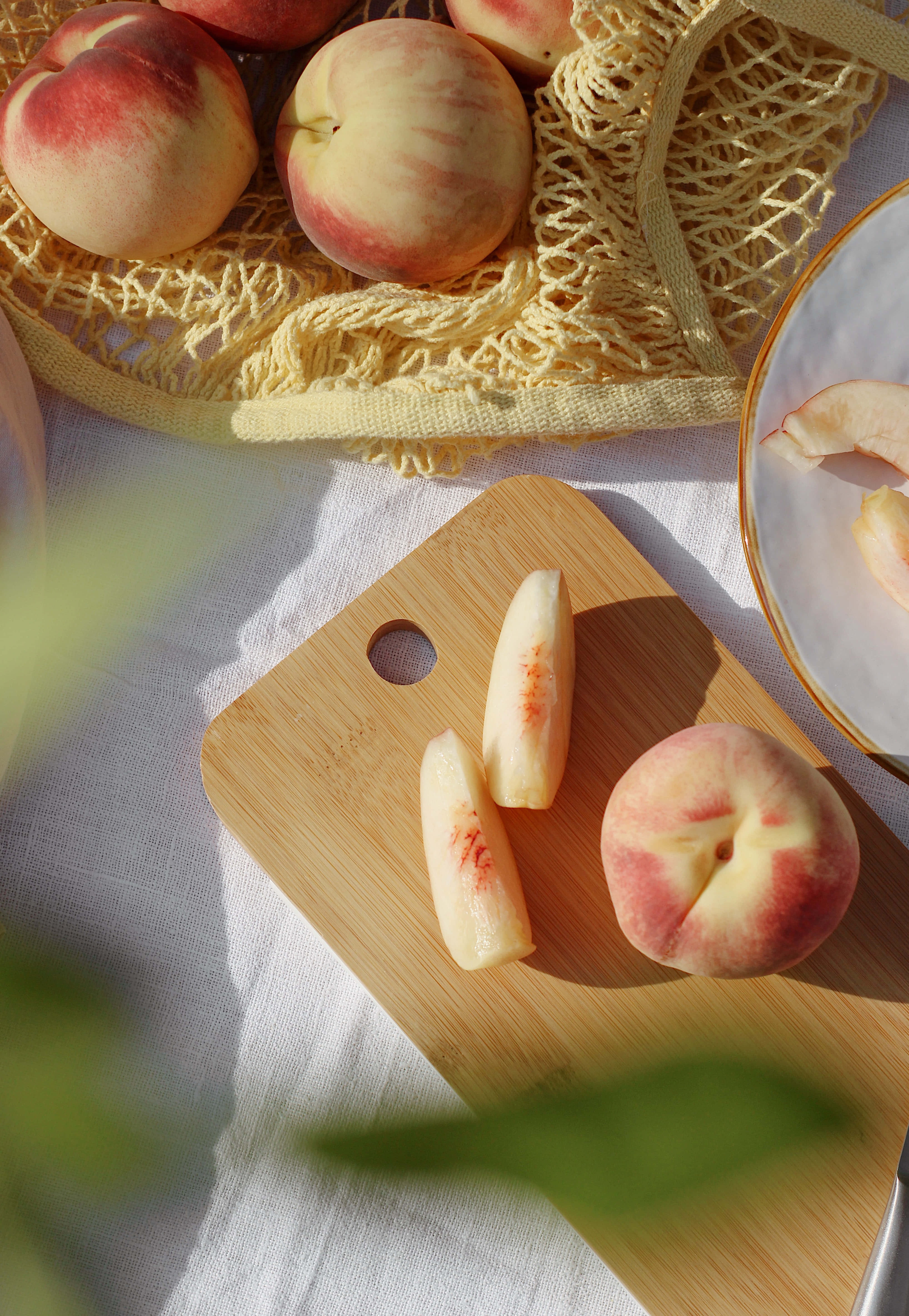 Peaches 桌布 壁紙 — 成熟的水蜜桃放在編織籃和木砧板上，在溫暖陽光下帶有柔和陰影。