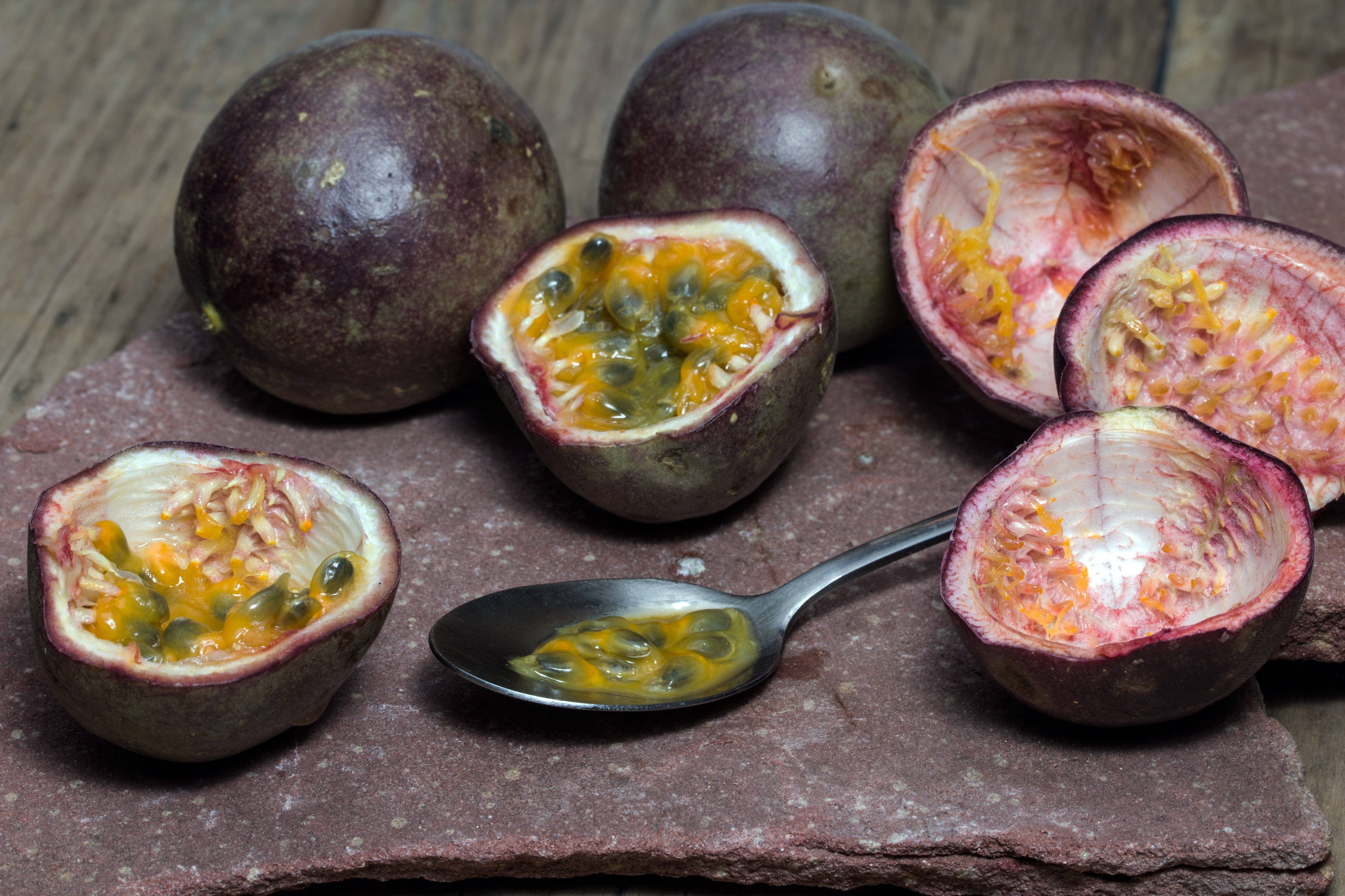 Passion Fruit 桌布 壁紙 — 成熟的百香果切開，露出多汁的橙色果肉和黑色種子，放在粗糙的石頭表面上。