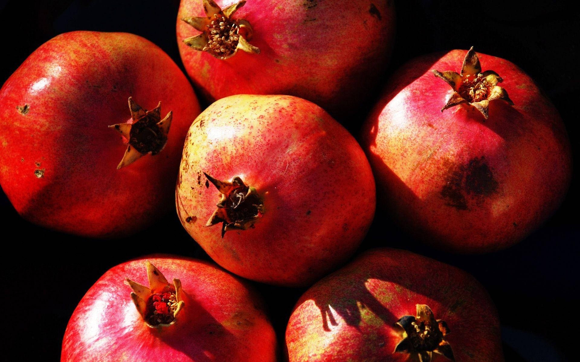 Fruits 桌布 壁紙 — 成熟的石榴，帶有紋理的紅色外皮和皇冠狀的莖，在戲劇性燈光下在黑暗背景中閃耀。