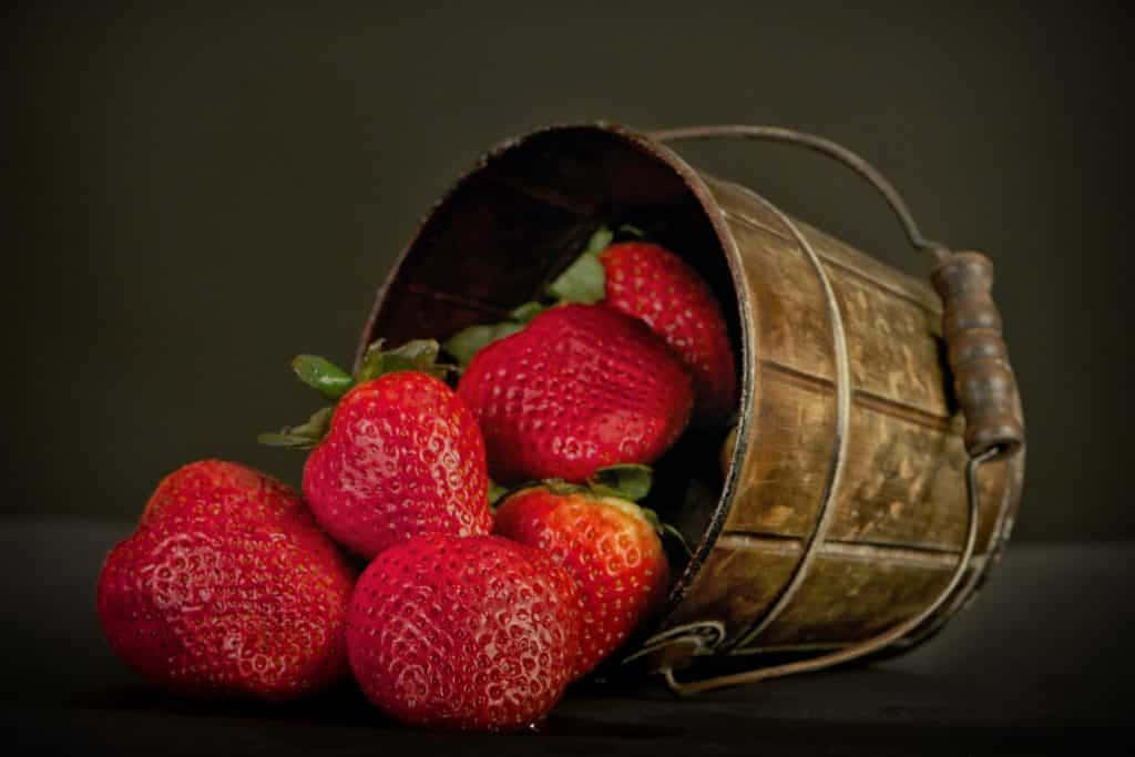 Strawberries 桌布 壁紙 — 成熟的紅色草莓從一個質樸的金屬桶中溢出，背景是陰暗的氛圍。