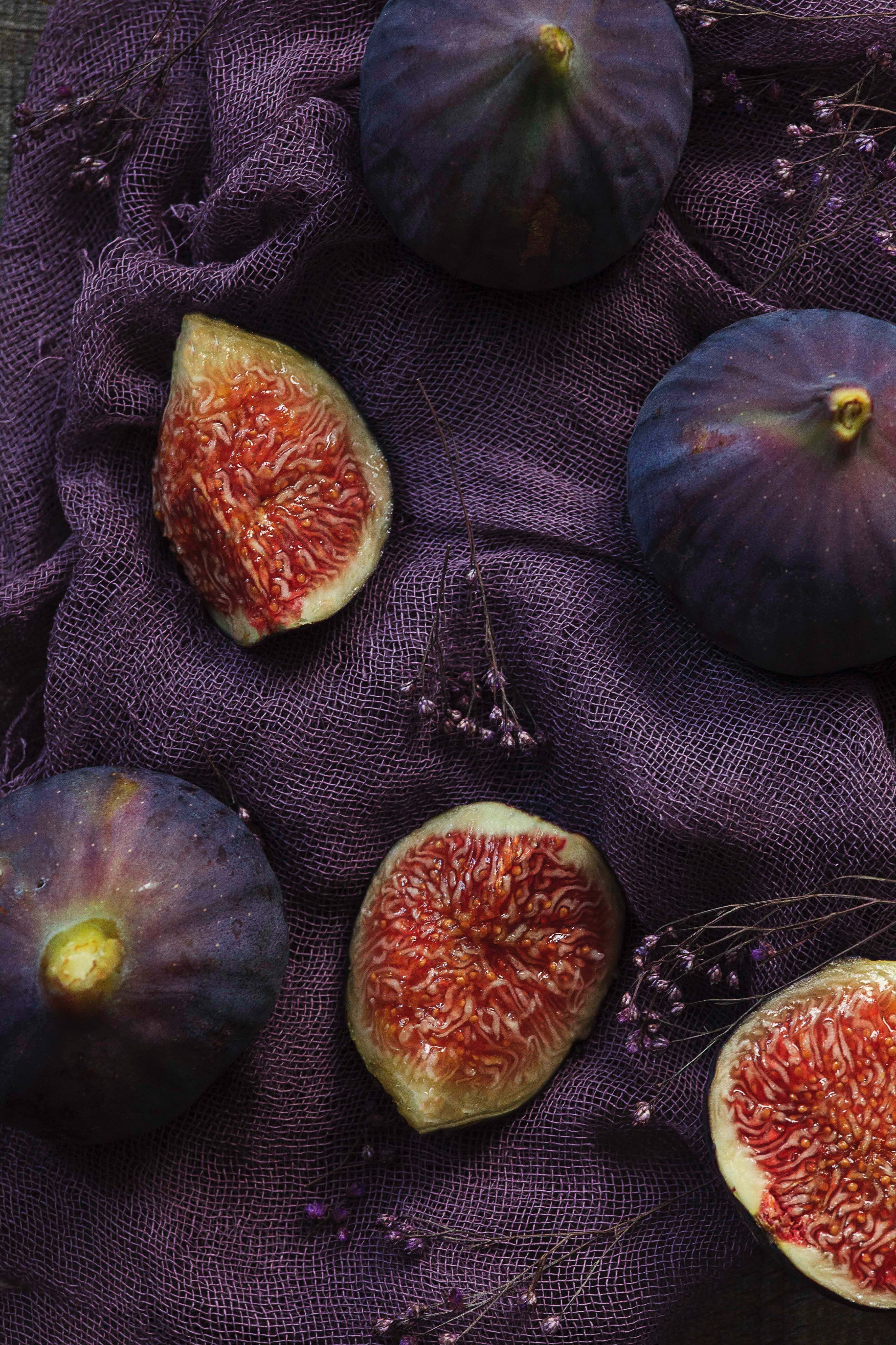 Purple Figs 桌布 壁紙 — 成熟的紫色無花果切開，露出多汁的紅色內部，放在有紋理的深紫色布料上。