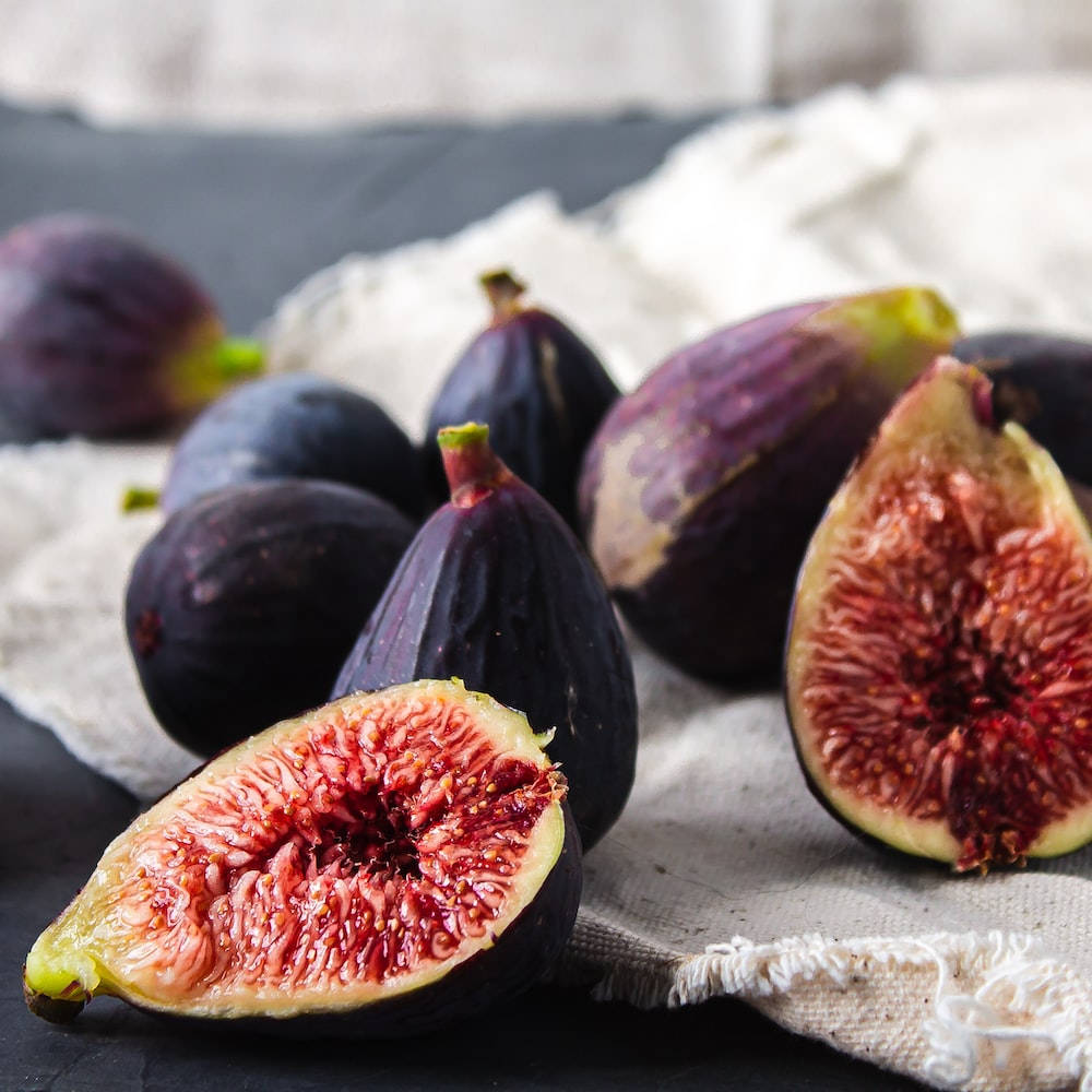 Fruit 桌布 壁紙 — 成熟的紫色無花果切開，露出多汁的紅色果肉，放在有紋理的白色布上，背景為深色表面。