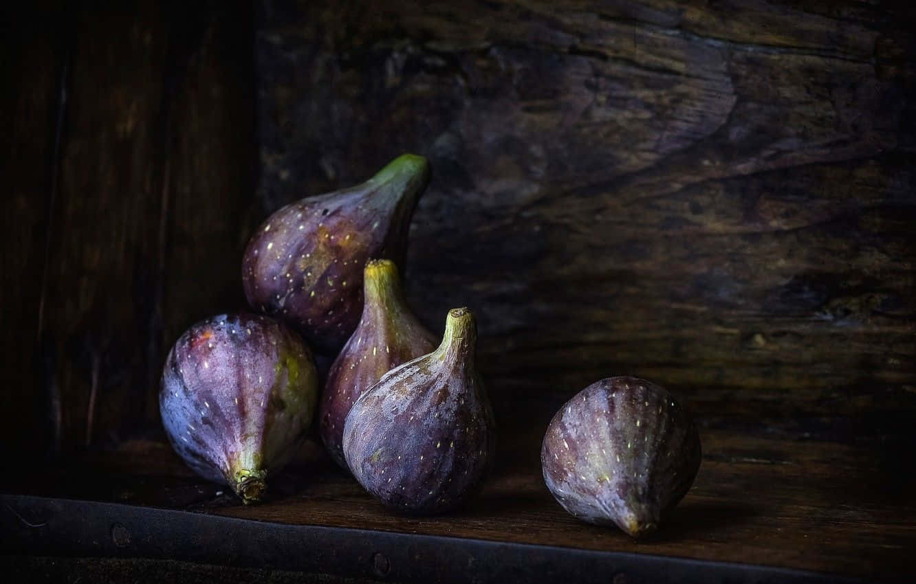 Purple Figs 桌布 壁紙 — 成熟的紫色無花果帶有斑點皮，放在深色木質表面上，背景是質樸的木頭。