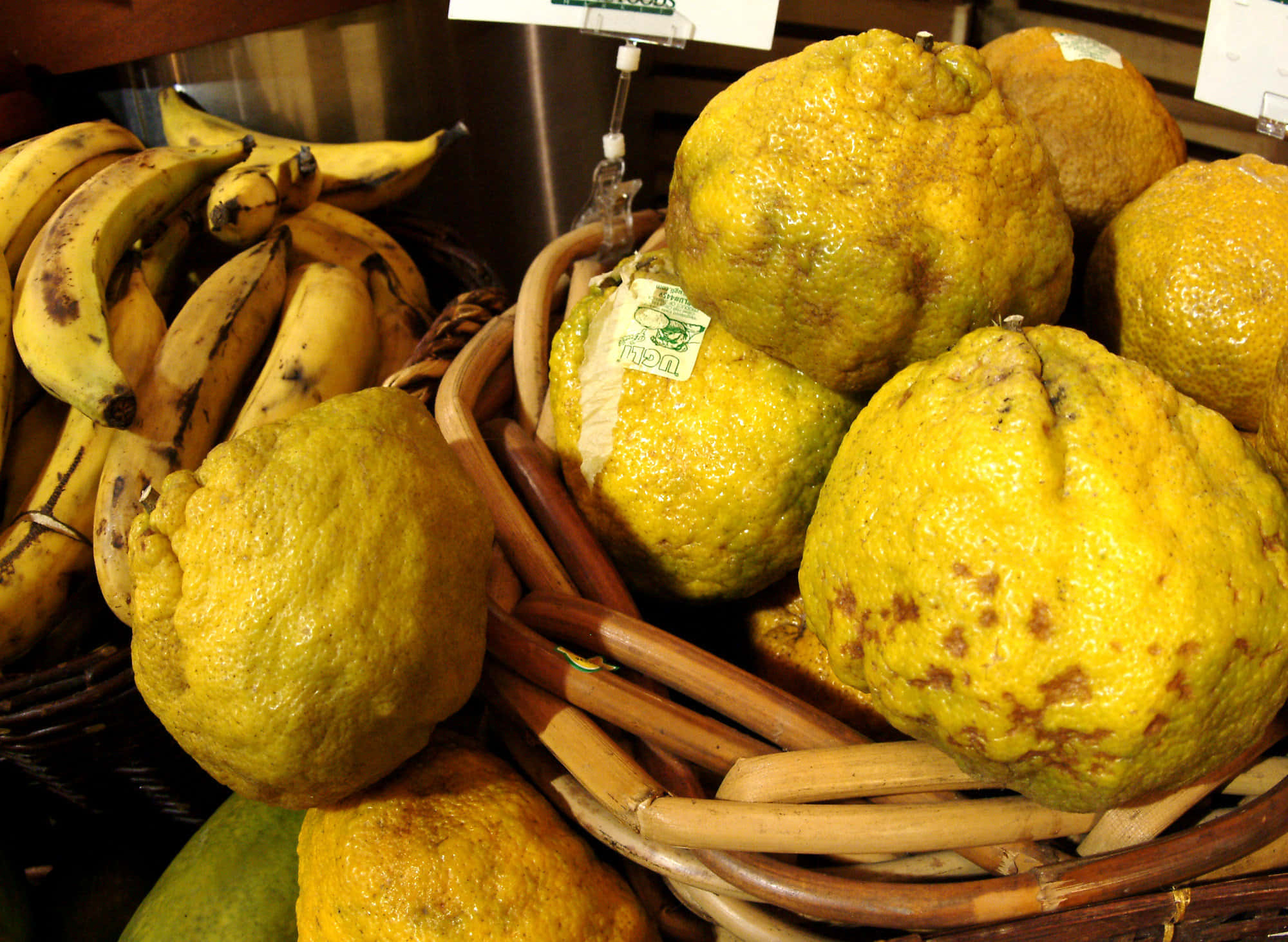 Fruits 桌布 壁紙 — 成熟的黃色柚子及有斑點的香蕉放在市場攤位的編織籃中，在溫暖燈光下。