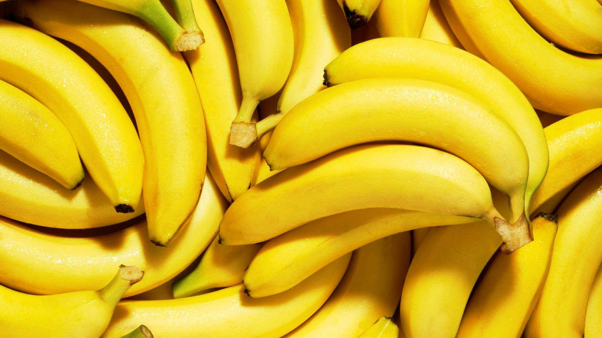 Plantain 桌布 壁紙 — 成熟黃色香蕉堆疊在一起的近距離特寫，表皮光滑，帶有綠色莖部。