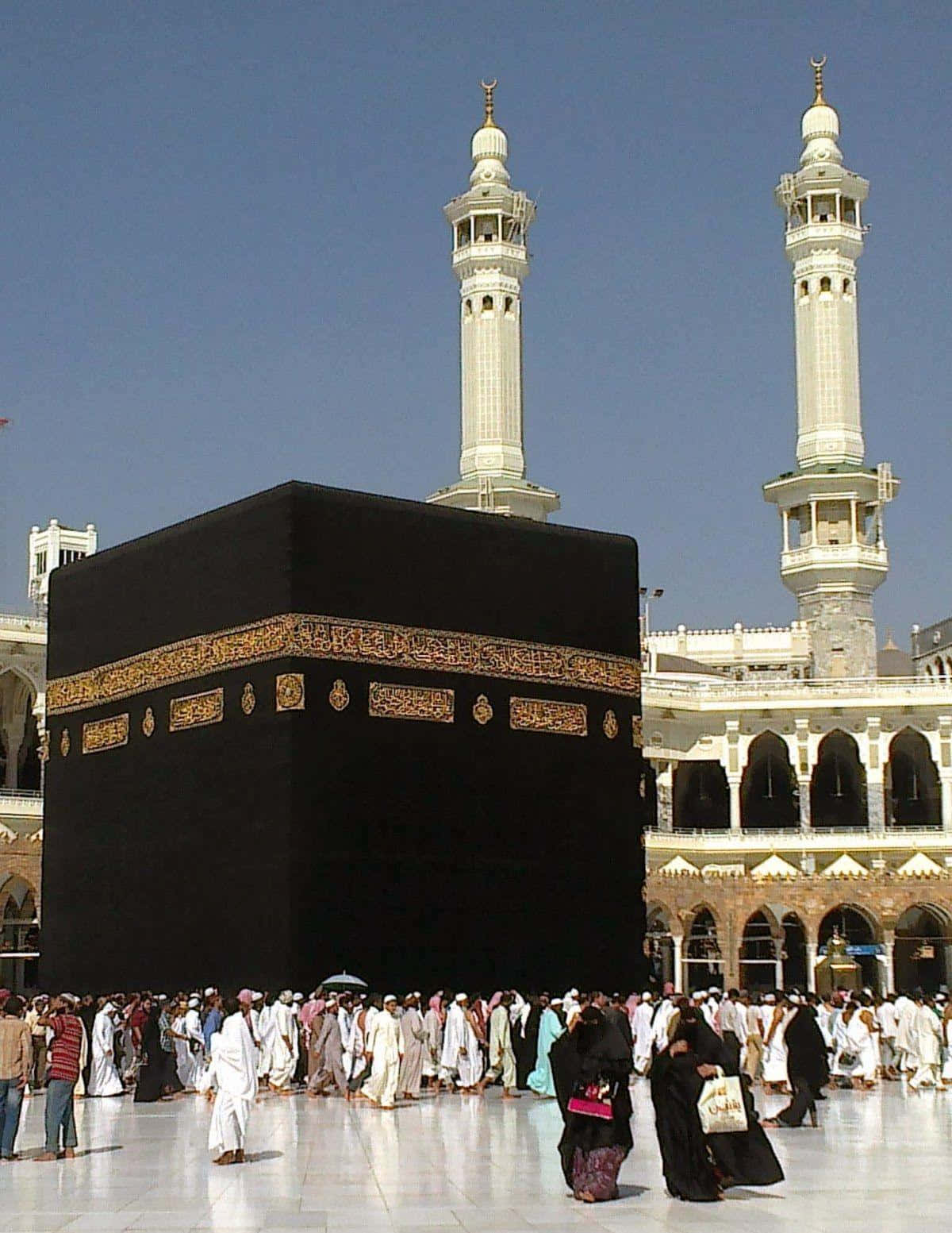 Kaaba 桌布 壁紙 — 成群朝聖者在晴朗藍天下繞行黑色天房，兩旁有兩座高大的白色宣禮塔。