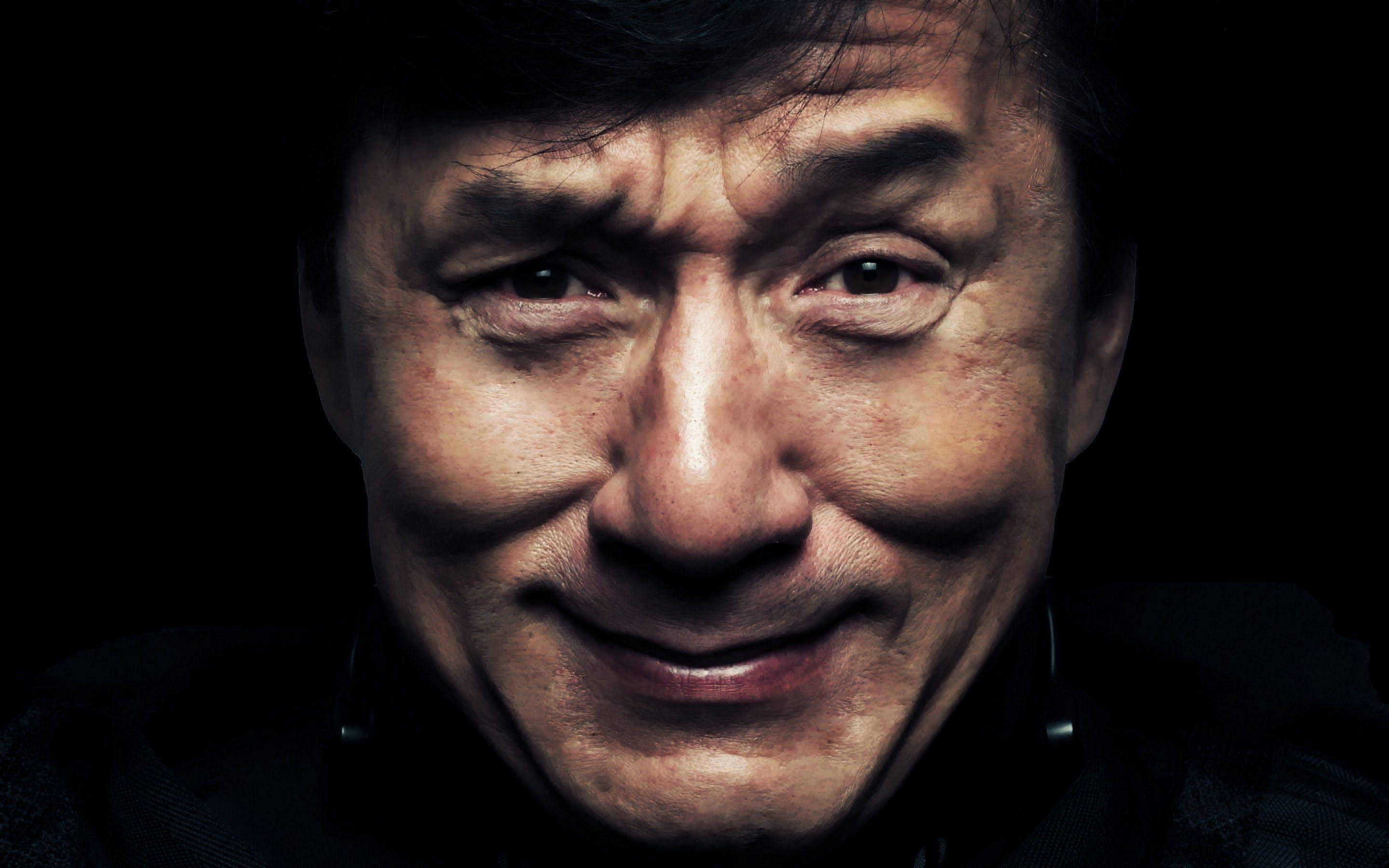 Face 桌布 壁紙 — 成龍的特寫肖像，帶著溫暖的笑容，背景是純黑色。