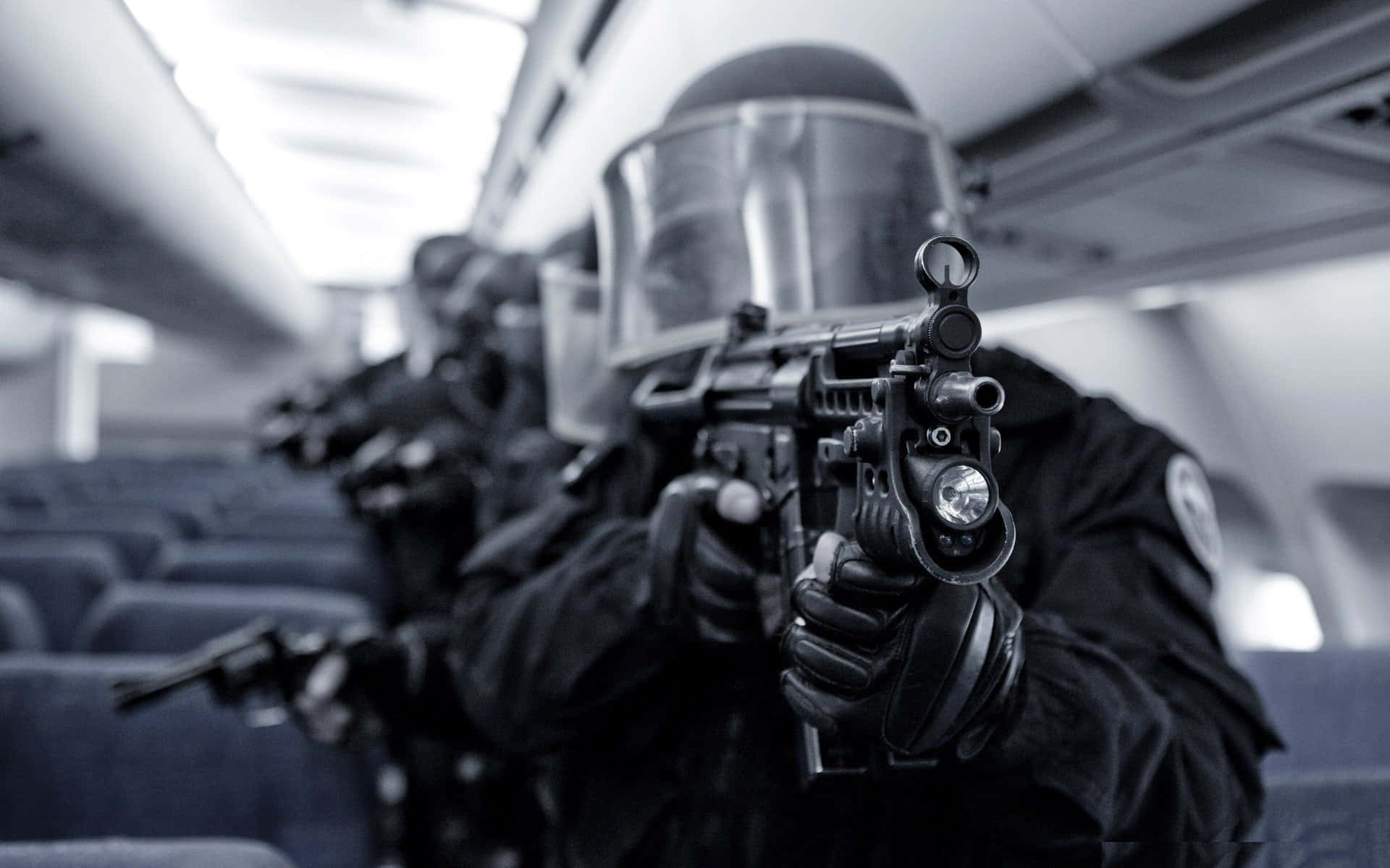 cop 桌布 壁紙 — 戰術警察穿著防暴裝備，手持步槍，在高對比黑白畫面中穿過飛機機艙。