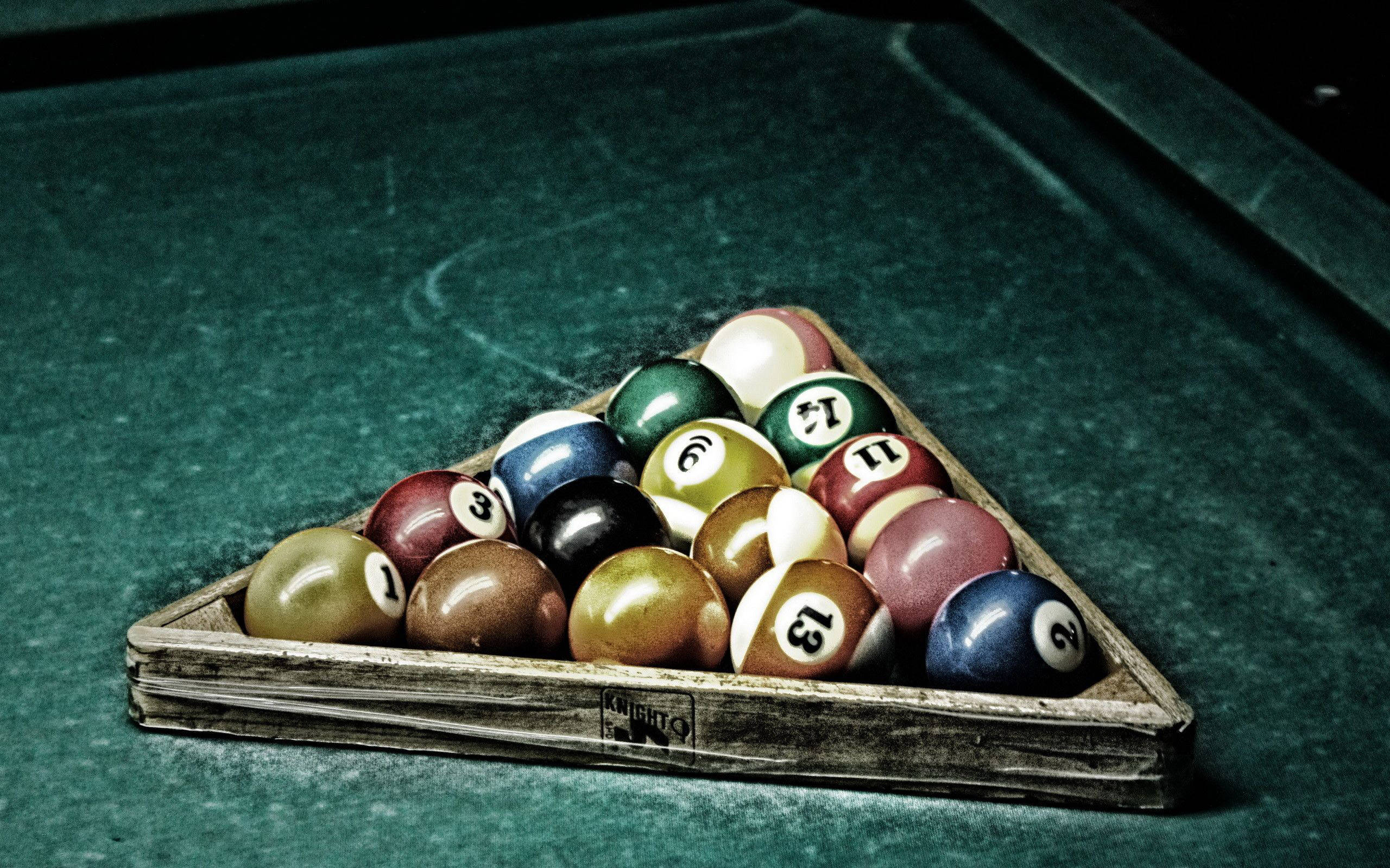 Snooker 桌布 壁紙 — 戲劇性燈光下，一個木製三角框內排列著色彩繽紛的撞球，放在磨損的綠色撞球檯上的特寫。