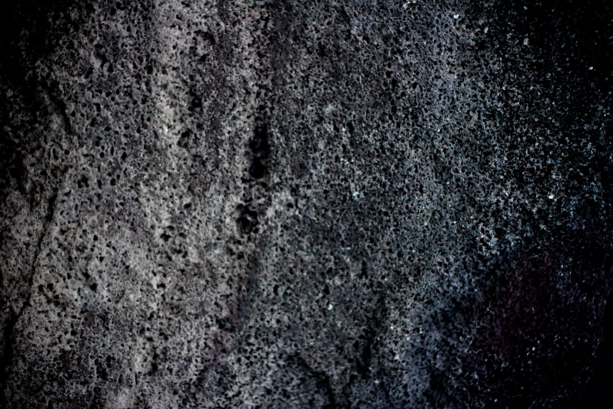 Dark Rock 桌布 壁紙 — 戲劇性燈光下粗糙火山岩表面的特寫，具有多孔紋理和深灰色調。