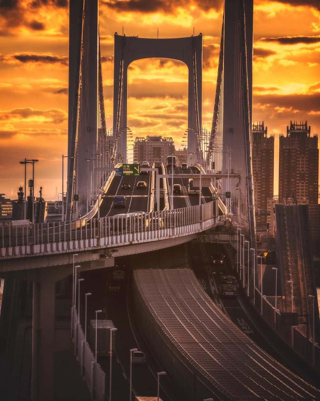 Rainbow Bridge 桌布 壁紙 — 戲劇性的夕陽將東京的彩虹橋沐浴在金色光芒中，車輛在繁忙的城市高速公路上的橋樑跨度上流動。
