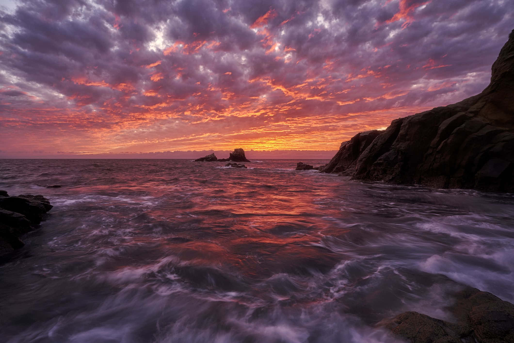 Beautiful Ocean 桌布 壁紙 — 戲劇性的夕陽將海洋和天空染成火熱的橙色和紫色，海浪拍打著崎嶇的懸崖。